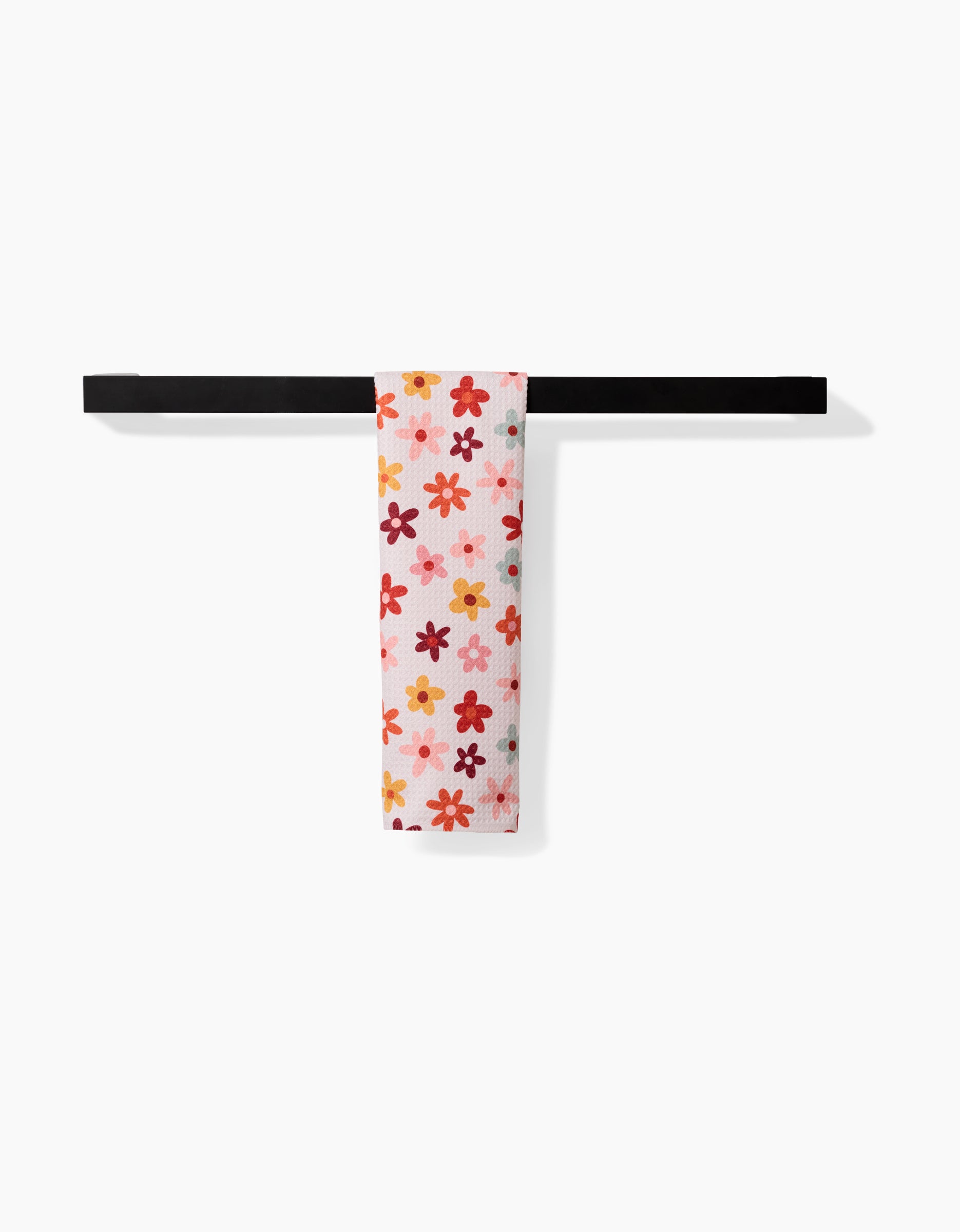 The Sara Mari Bright Field Of Fall Daisies towel, ultra-absorbent and white with a vibrant red, orange, and pink floral pattern, is neatly displayed on a simple black rack against a plain white background.