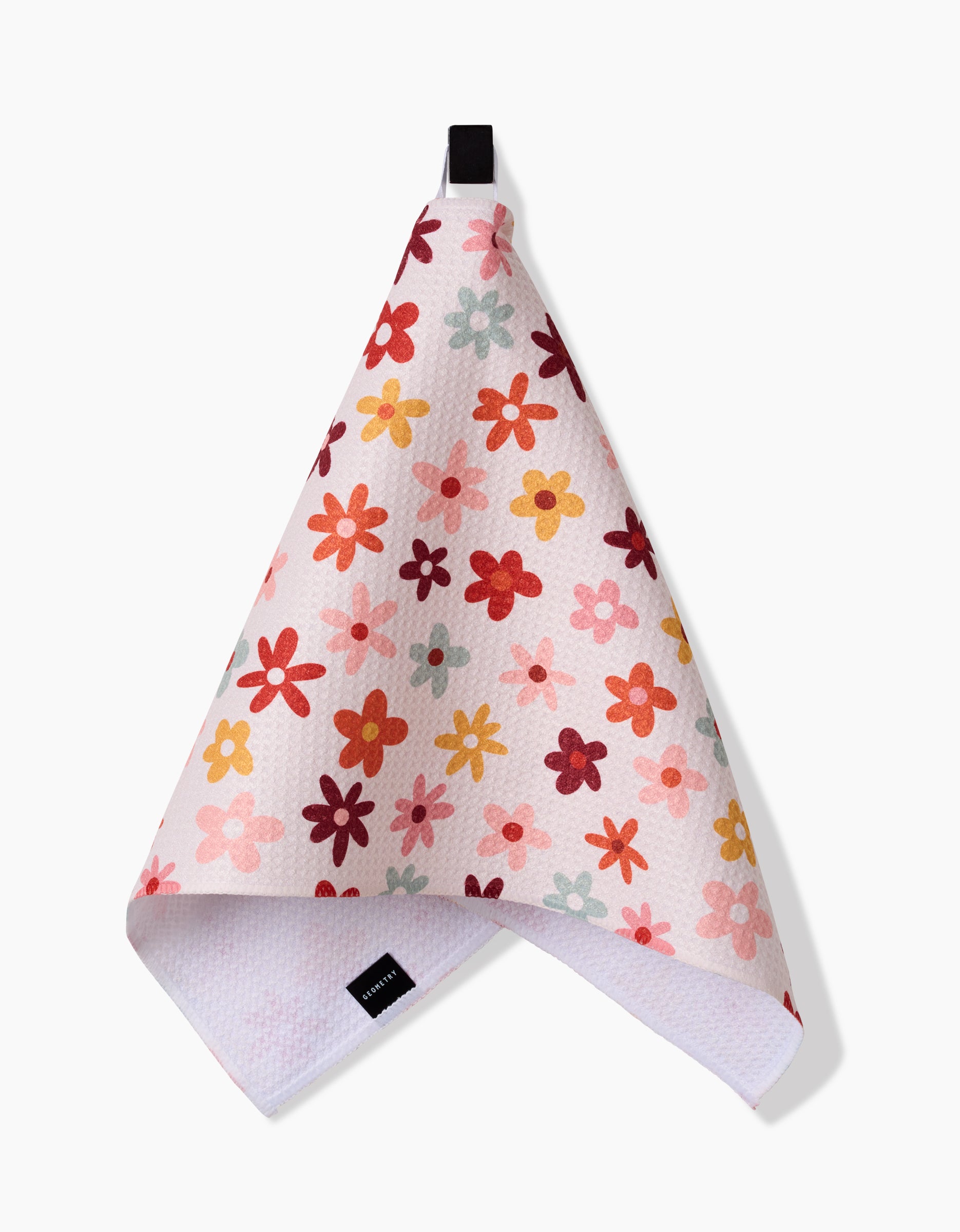 The Sara Mari Bright Field Of Fall Daisies towel is ultra-absorbent and white, featuring a colorful floral pattern in red, orange, yellow, and pink with a textured surface. It hangs by a black loop and has a visible fabric tag at the bottom.
