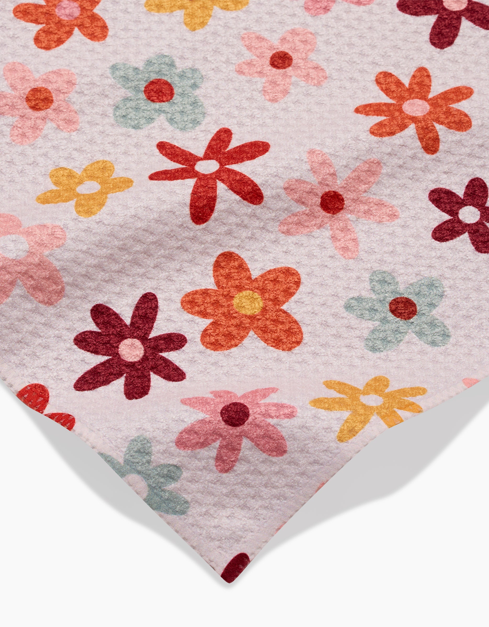 A close-up of Sara Mari’s Bright Field Of Fall Daisies towel, an ultra-absorbent white towel adorned with a textured surface and a vibrant floral pattern in red, orange, yellow, pink, and green.