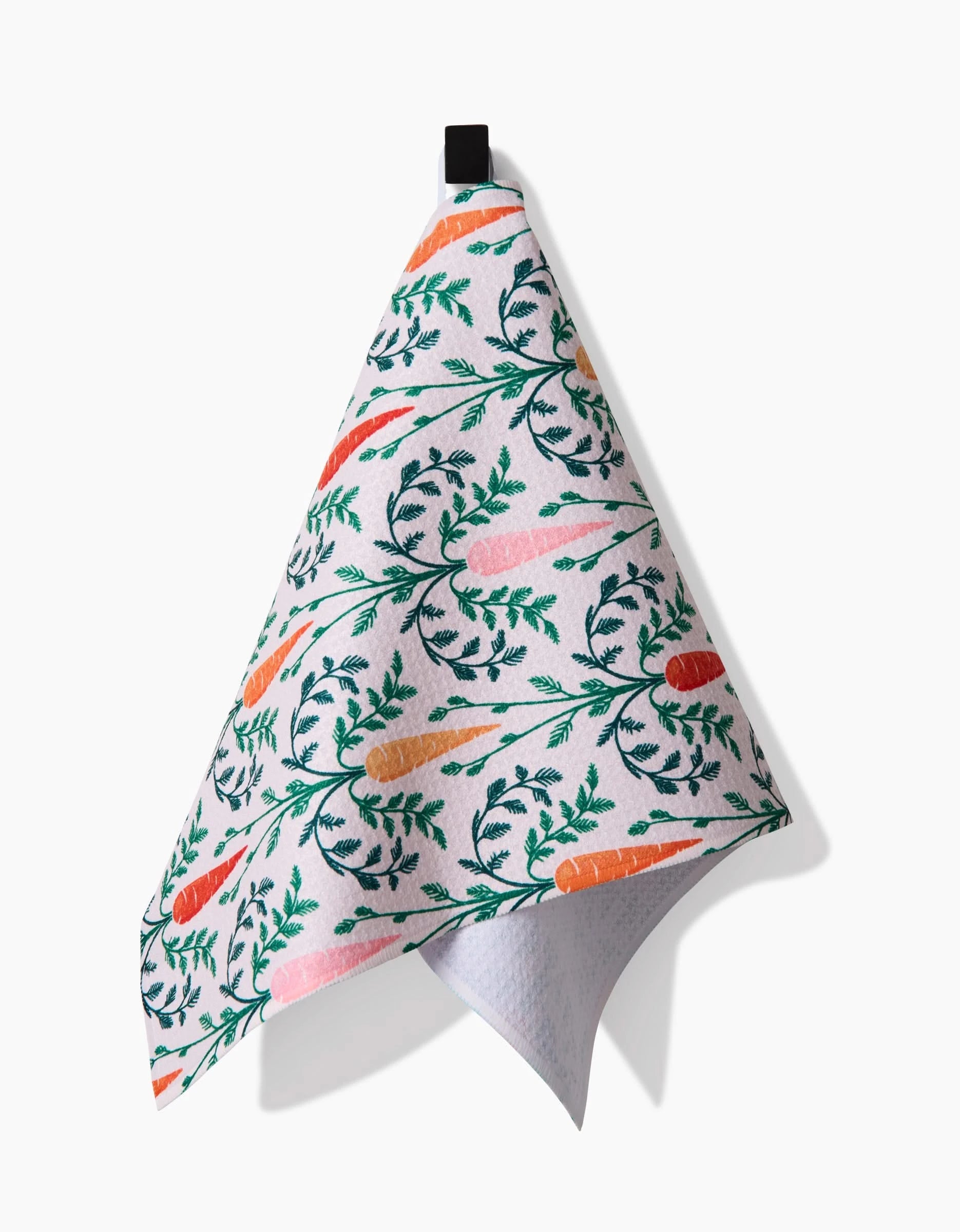 The Sarah Daugherty Carrot Damask recycled kitchen towel, featuring a colorful carrot and green leaf pattern, hangs from a black loop against a plain white background.