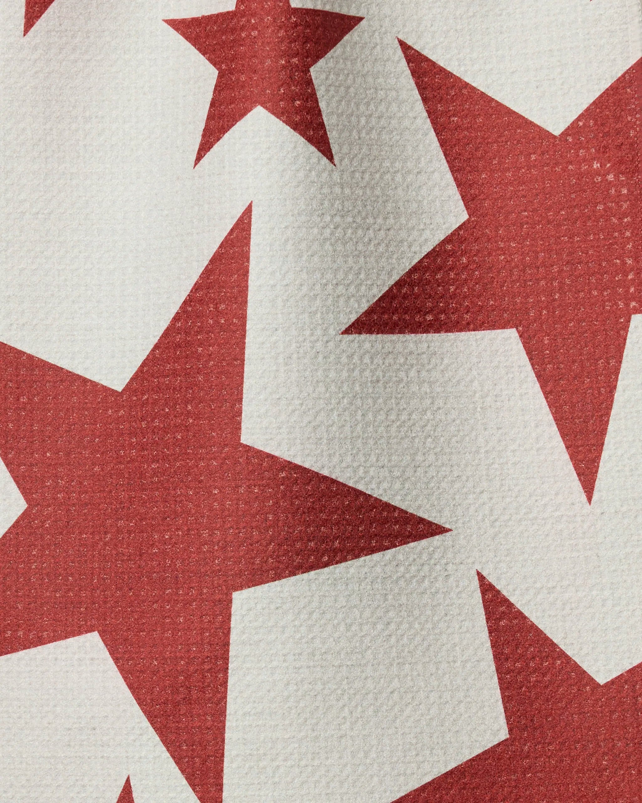 A close-up of Geometry's Celestial recycled kitchen towel shows a textured white surface with a pattern of large and small red stars, some partially visible at the edges.