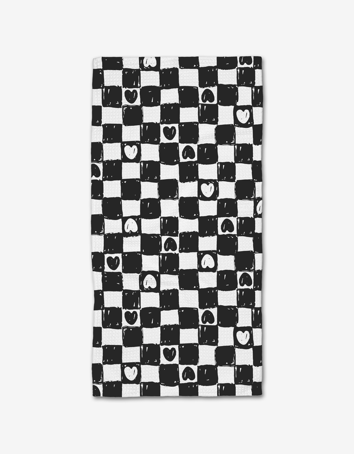 Checkered Hearts by Hufton Studio features a hand-drawn black and white checkered pattern with uneven lines, hearts, and smiley faces. This playful design is printed on a Geoweave bar towel made from post-consumer recycled materials.
