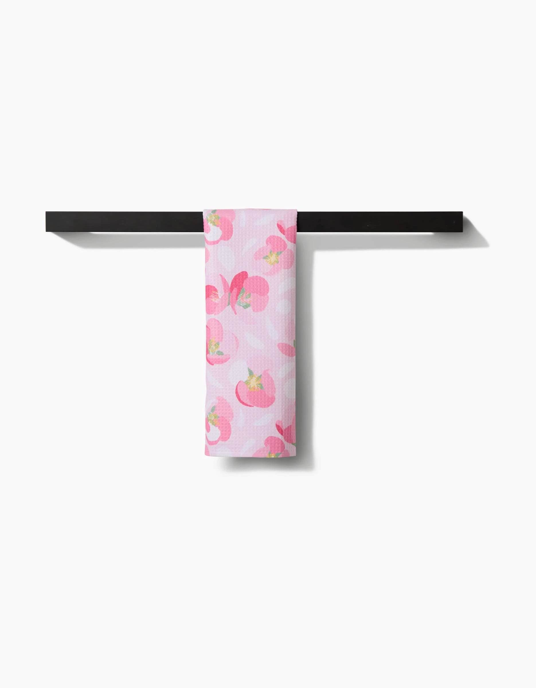 The Cherry Blossom Bar Towel by Rebecca Bobko, made from Geoweave fabric, displays red and pink floral patterns and hangs over a black towel rack against a white background.