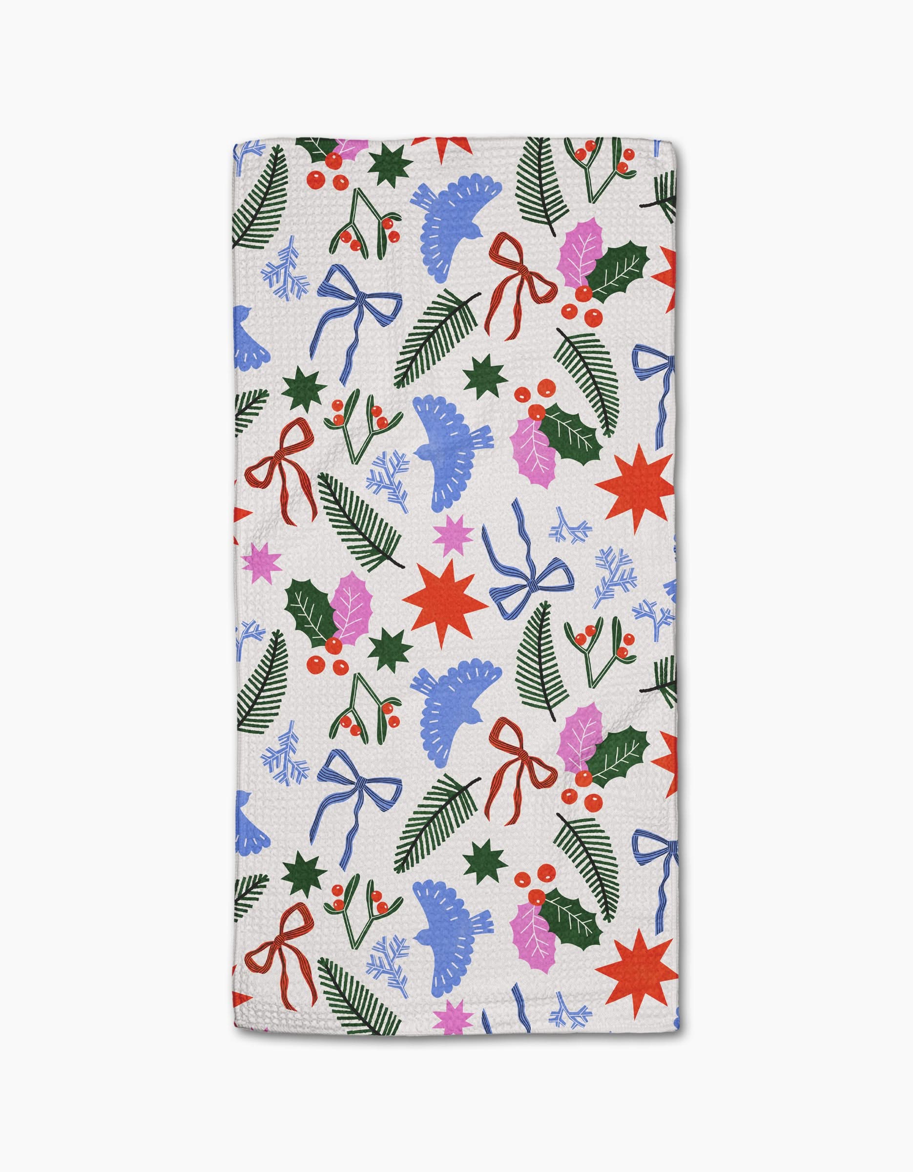 The Claire Iglesias Christmas Garden Party towel is ultra-absorbent and white, featuring a festive design with red bows, holly leaves and berries, pine branches, blue flowers, red stars, and purple leaves.