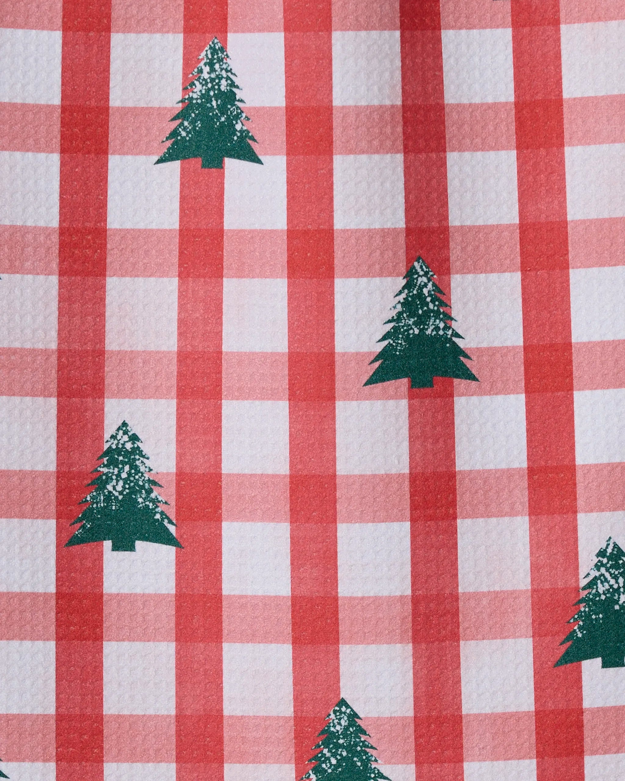 Christmas Pines by Geometry features red and white checkered fabric made from recycled materials, with a repeating pattern of green pine trees spaced apart and a slightly textured surface.