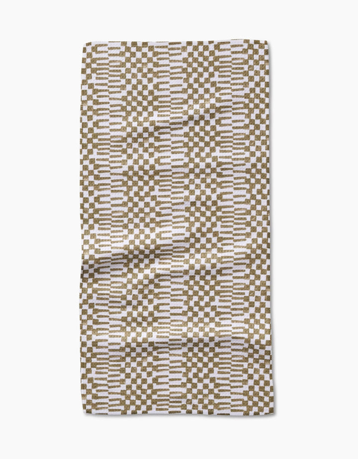 The Studio Jeannot Chutes Avocado is a rectangular bar towel made from Geoweave fabric, featuring a geometric pattern of brown and white rectangles with horizontal white lines on a neutral background. It is shown slightly wrinkled on a white surface.