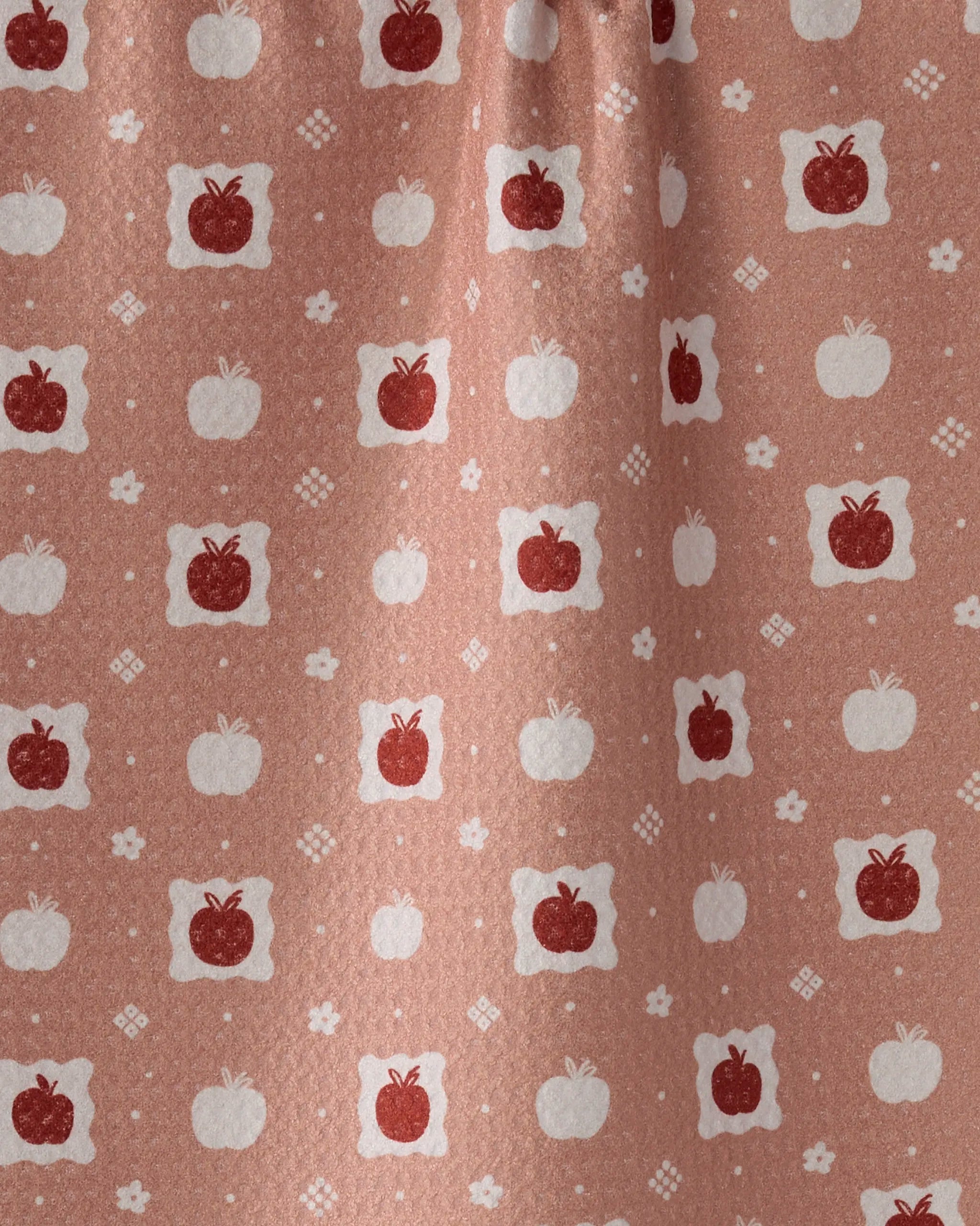 The Cider Mill curtain by Geometry is made from recycled materials in a pinkish-brown fabric. It features soft folds, a matte texture, and a repeating pattern of red and white apples, white flowers, and geometric shapes.