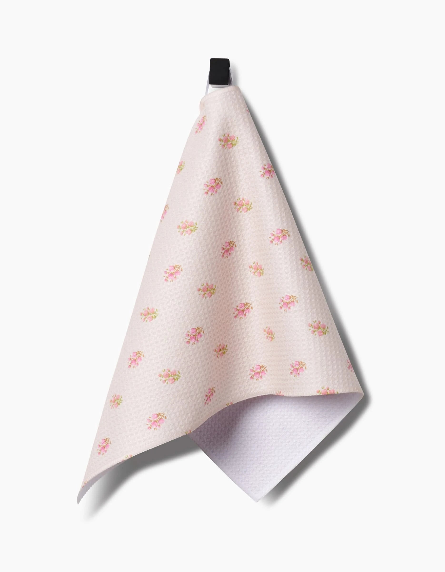 The Cindy bar towel by Kelsi Fullmer features pink textured fabric with small yellow and pink floral patterns, made from recycled materials, and hangs from a black loop against a white background.