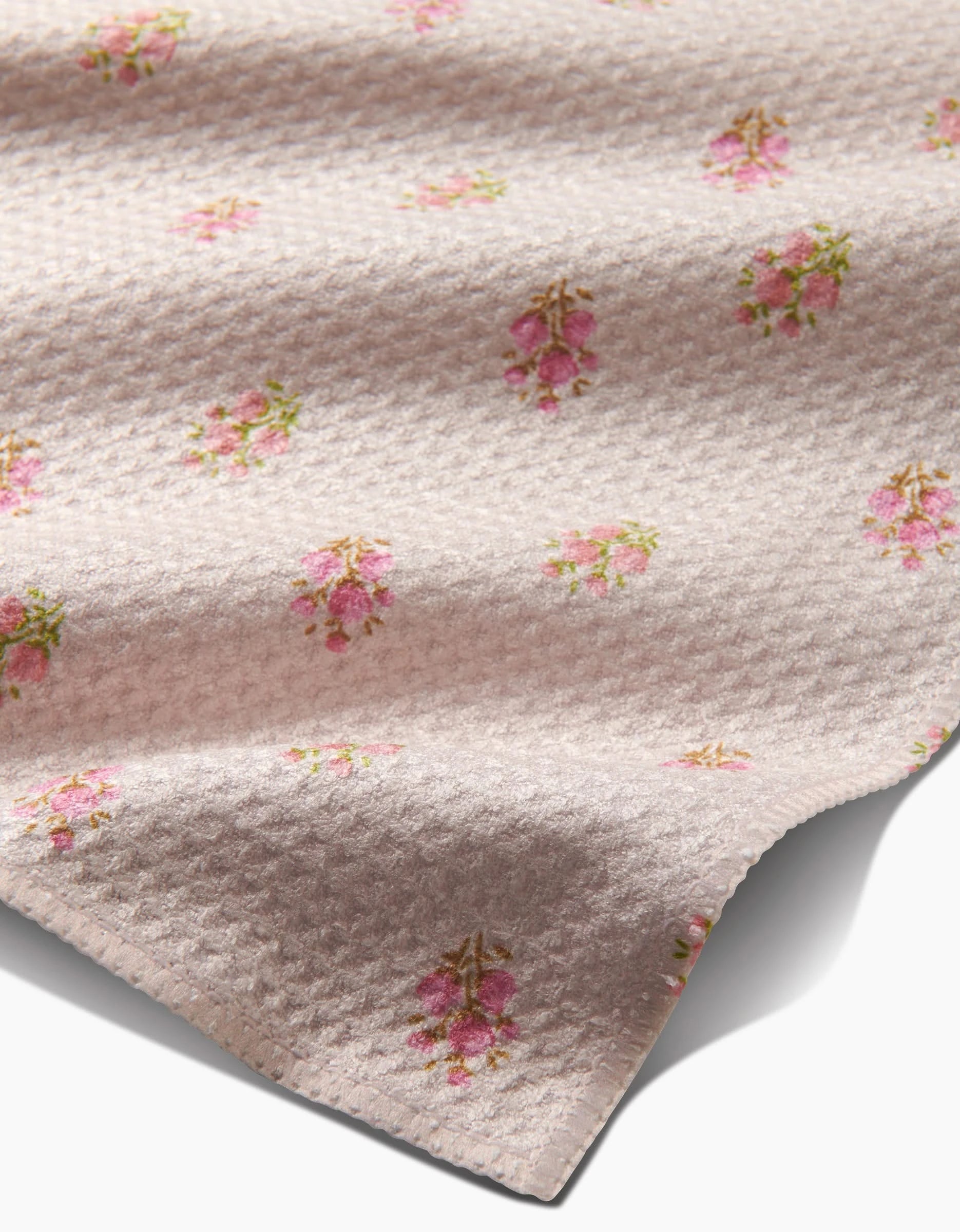 A close-up of textured, light pink Geoweave fabric from Kelsi Fullmer’s Cindy bar towel shows clusters of pink flowers and green leaves in a repeating pattern, with the towel’s edge visible in the lower right corner.