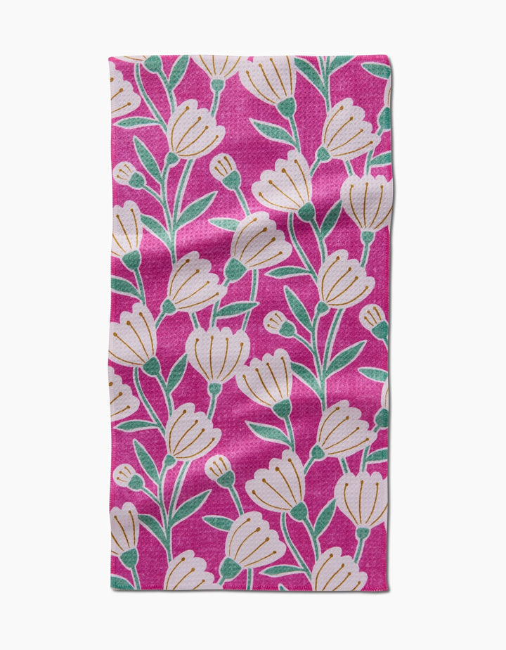The Clemmie Bar Towel by Amy MacCready is a rectangular pink Geoweave towel with a repeating pattern of white flowers, green stems, and leaves evenly spread for both style and durability.