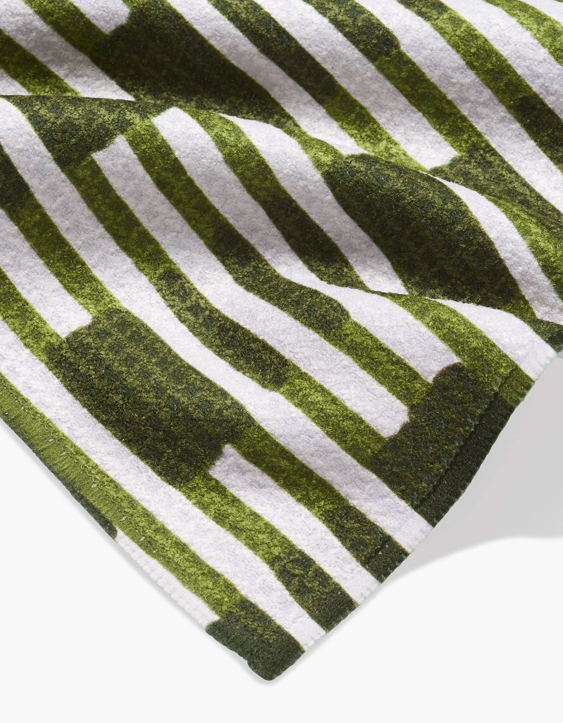 A close-up of GEOMETRYs Clover Stripe quick-drying towel fabric, showing alternating green and white vertical stripes with irregular, blocky green shapes overlaid.