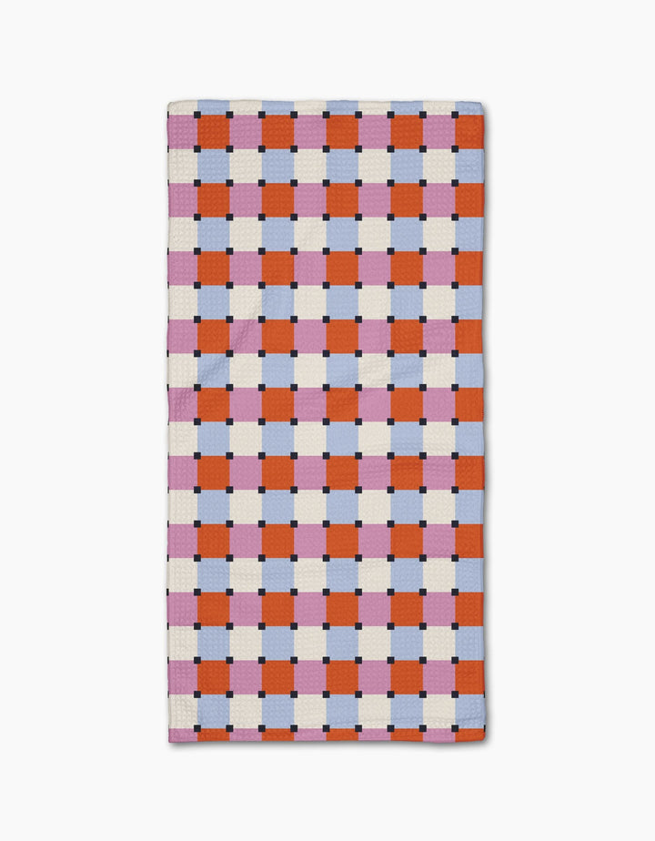 The Claire Iglesias Color Block Grid Bar Towel is crafted from Geoweave™ fabric and showcases an orange, pink, and white checkerboard pattern with blue and black accents on a crisp white background.