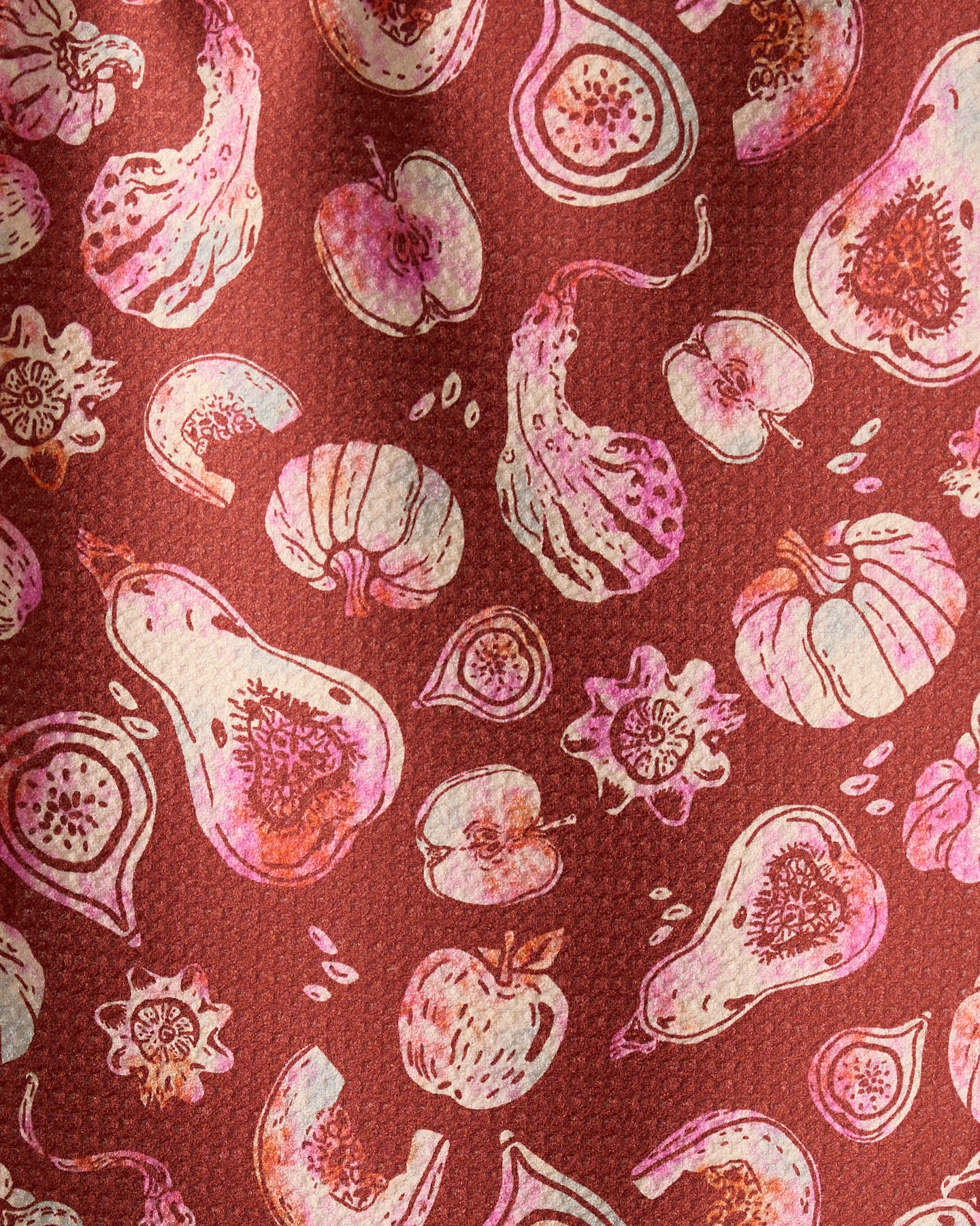 Geometry’s Cosecha bar towel features illustrations of fruits and vegetables—like gourds, figs, pumpkins, and apples—in pink and cream on a textured reddish-brown background. Made from ultra-absorbent recycled materials.