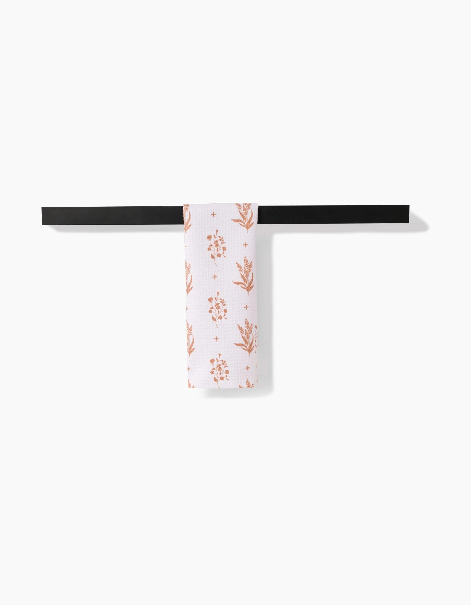 The Country Road bar towel by Charlie Rowan Designs features an orange floral pattern on white Geoweave fabric and hangs from a sleek black bar—a modern, versatile kitchen accessory that complements any contemporary space.
