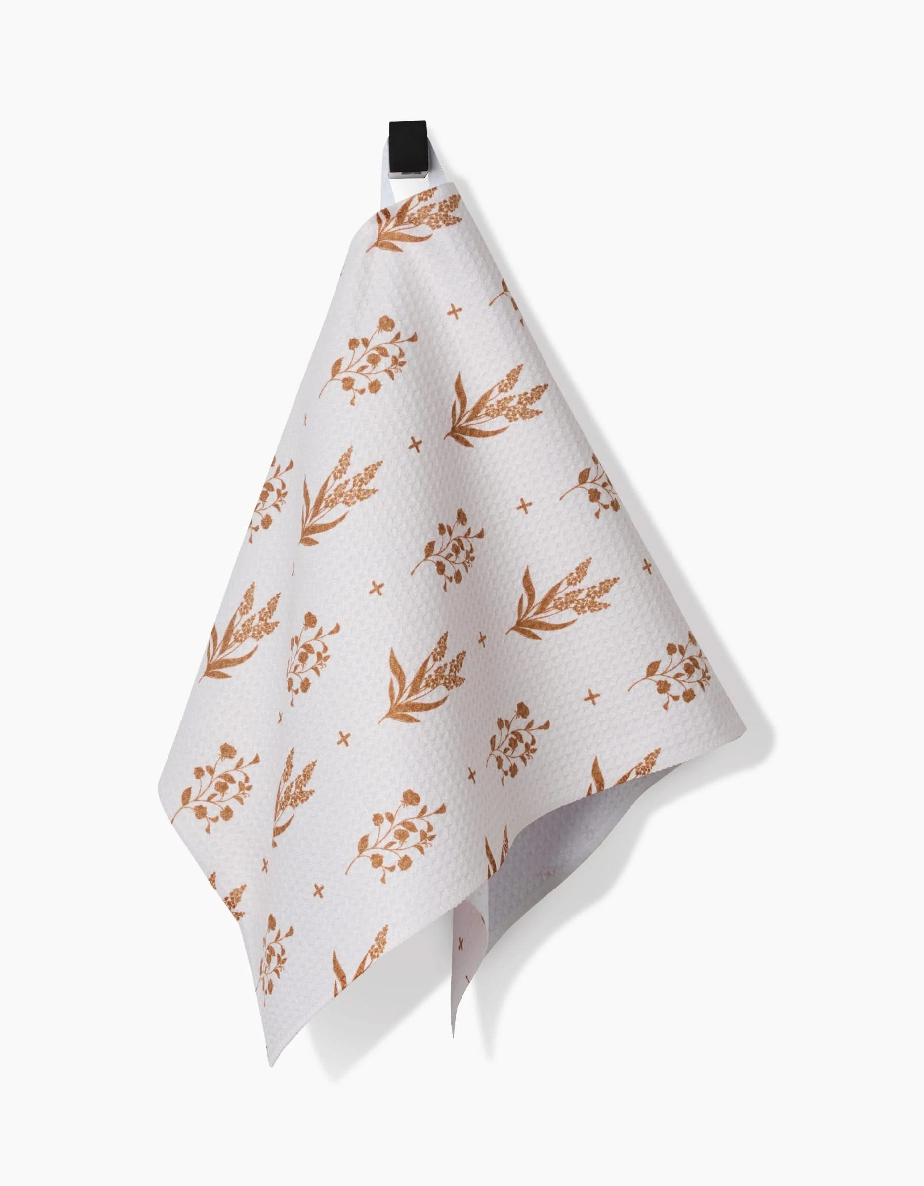 The Country Road bar towel by Charlie Rowan Designs features a brown floral and leaf pattern on white Geoweave fabric, hanging from a black hook against a white backdrop—a stylish and functional kitchen accent.