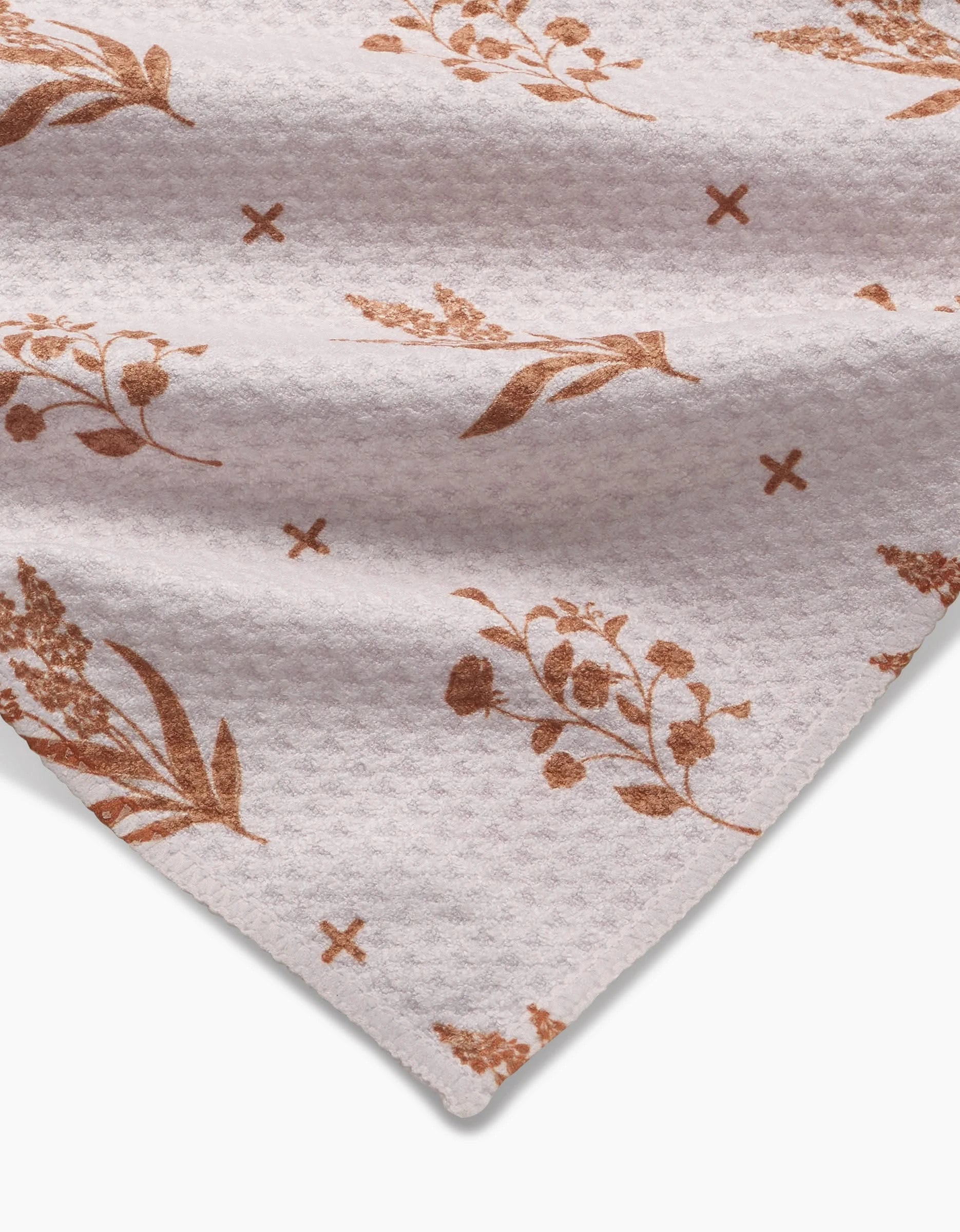 A close-up of the Country Road Geoweave bar towel by Charlie Rowan Designs, featuring brown floral and leaf patterns with small brown X marks on white fabric—an elegant angled view showing the corner.