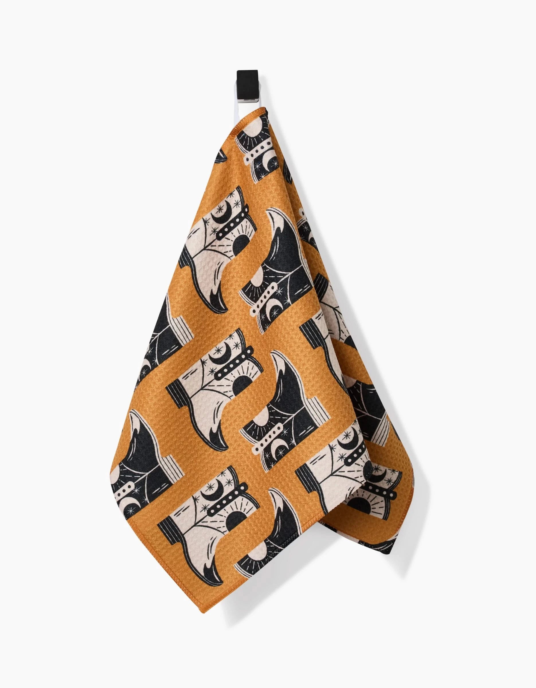 The Megan Roy Cowboy Boots bar towel features a repeating orange pattern of black and white cowboy boots. Made from ultra-absorbent recycled materials, it hangs by a black loop against a white background.