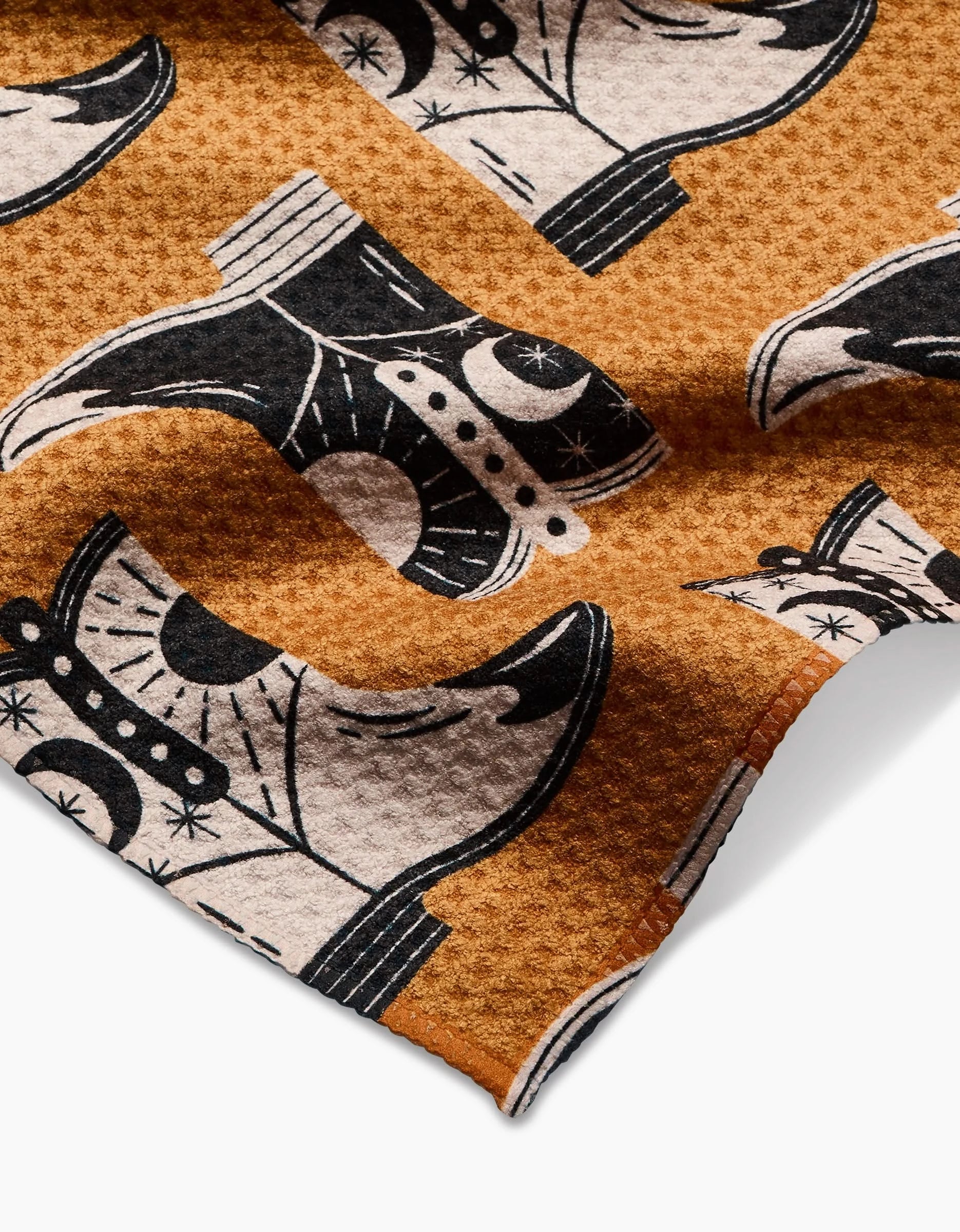 A close-up of Megan Roy’s Cowboy Boots bar towel, made from recycled materials and showcasing a textured orange surface with a repeating black-and-white stylized cowboy boots pattern.