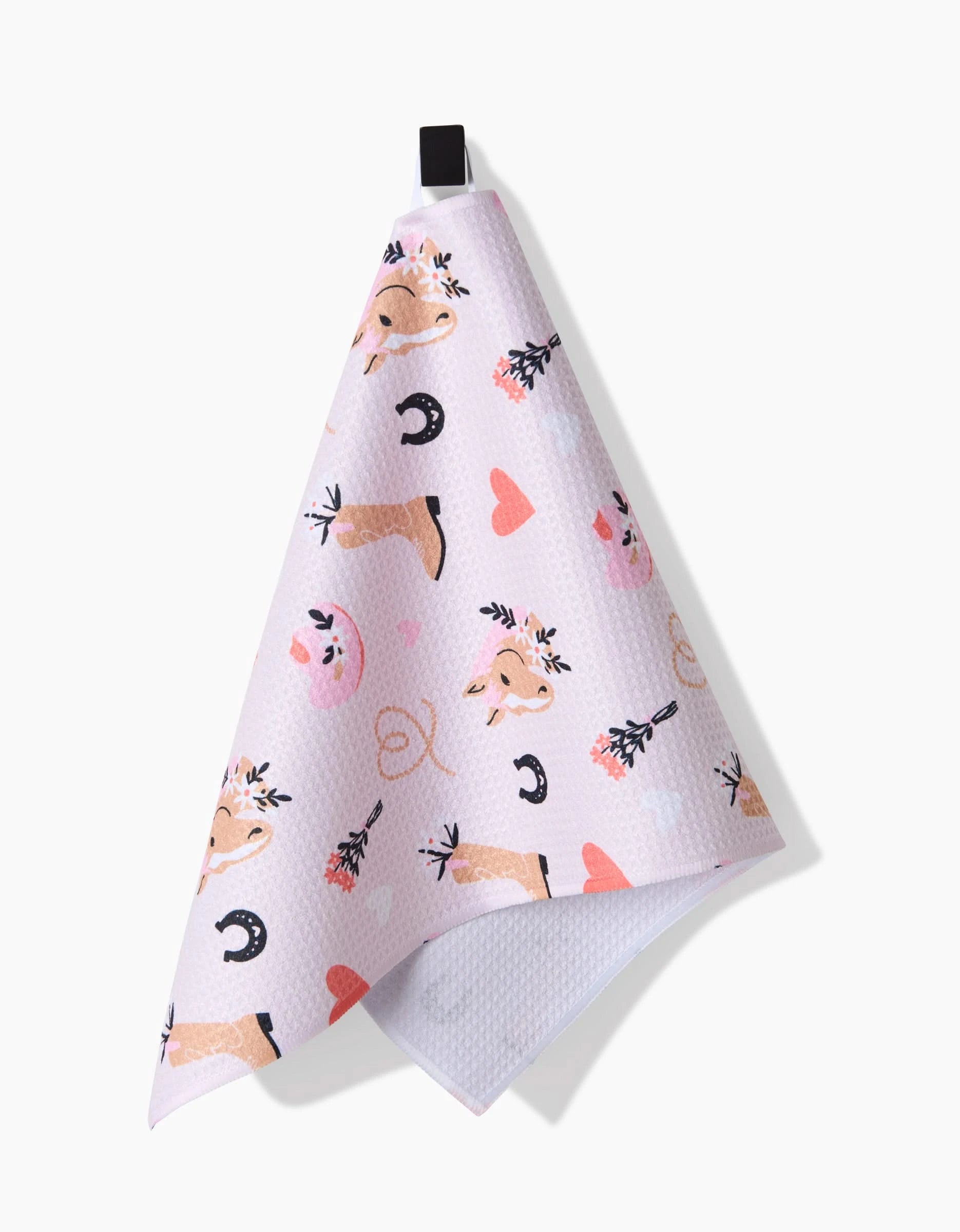 Amberleigh Adoffs Cowgirl Love pink ultra-absorbent bar towel features cowgirl-themed art—cow faces, horseshoes, lassos, boots with flowers, and hearts. Hang it by the black loop to add a Western touch to your kitchen.