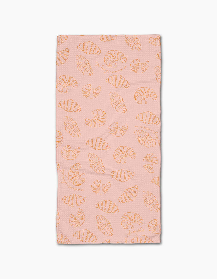 The Croissant Crush towel by Geometry is a pink rectangular bar towel with an all-over orange line-drawn croissant pattern, crafted from durable Geoweave fabric and displayed on a white background.