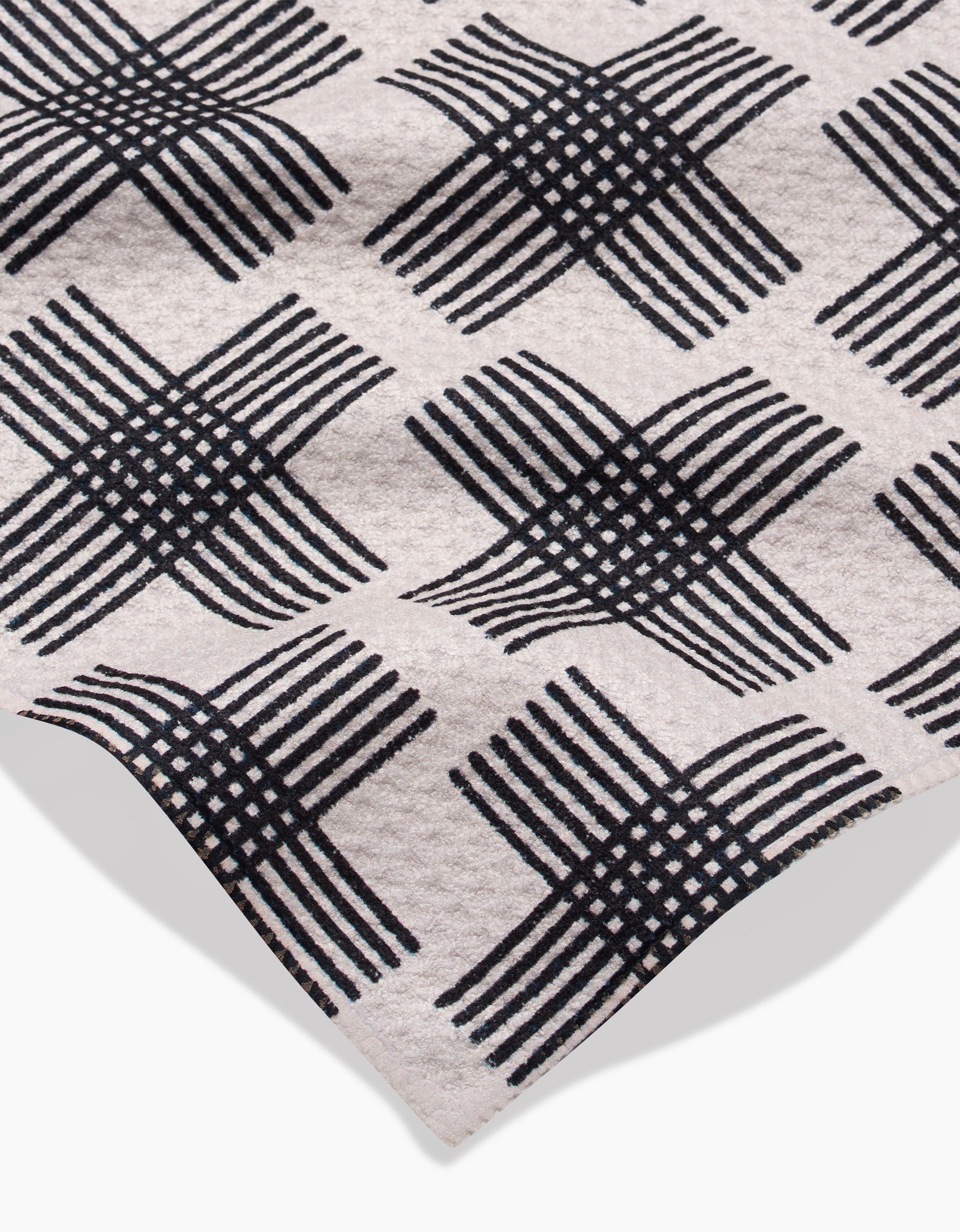 A close-up of Rosa Kichline’s Cross Hatch bar towel in beige Geoweave fabric, featuring a black diamond-patterned crisscross design. Made from post-consumer recycled materials with a folded corner and subtle texture.