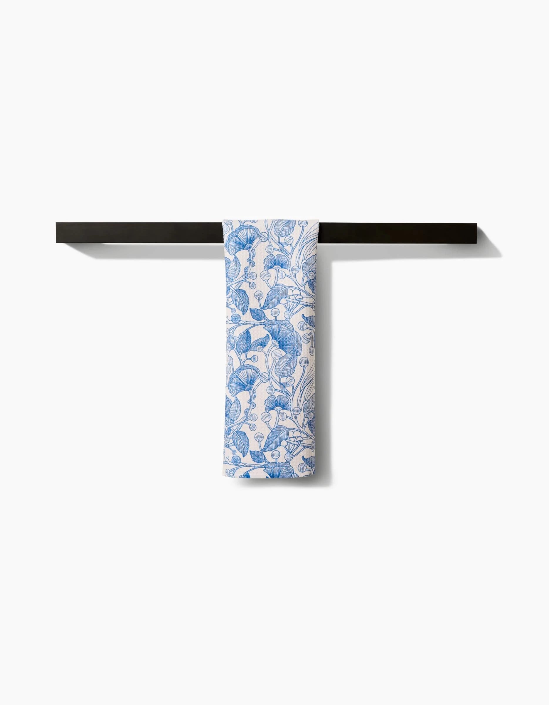 The Crowberries bar towel by Katie OShea, featuring a blue floral pattern on white Geoweave fabric, is neatly folded over a sleek black towel bar against a plain white background.