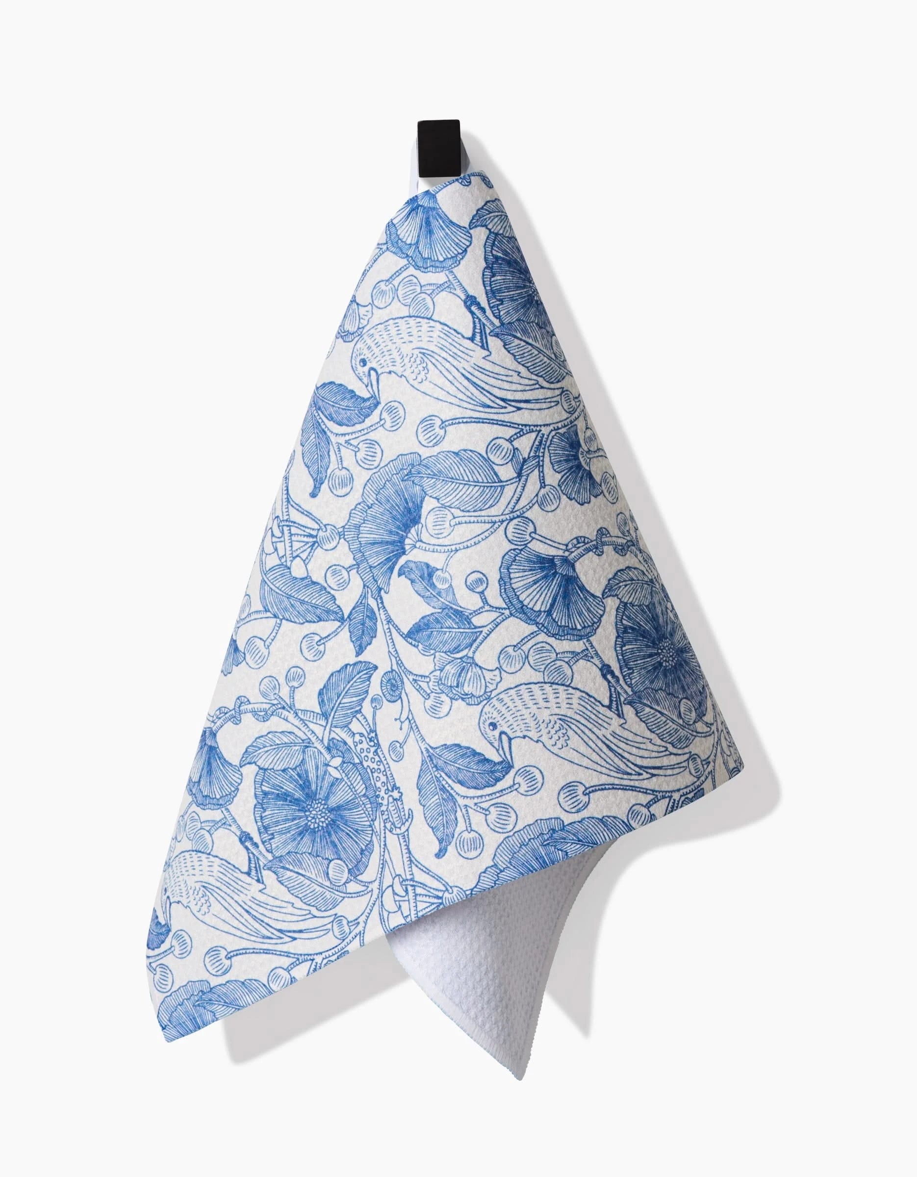 A white Crowberries bar towel by Katie OShea, featuring a blue botanical pattern of flowers and leaves on Geoweave fabric, hangs from a black hook and casts a shadow on the white background.