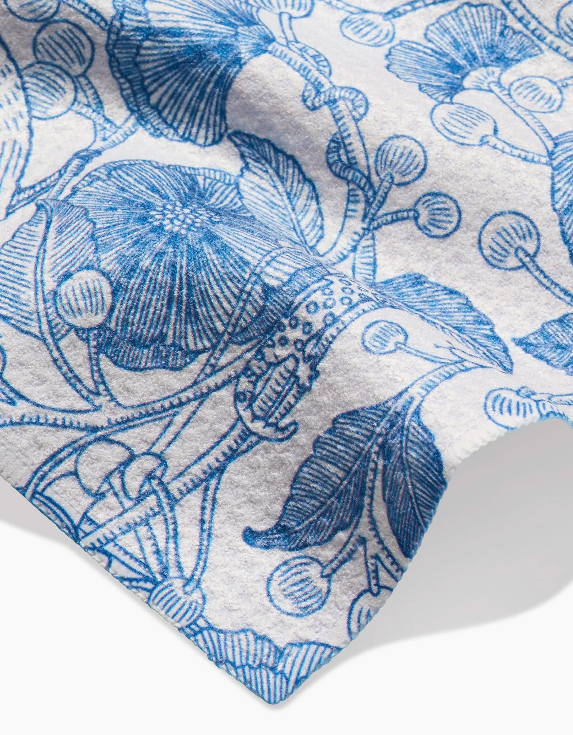 A close-up of the Katie OShea Crowberries bar towel shows its textured white Geoweave fabric, highlighted by an intricate blue floral design with leaves, flowers, and berries on a softly wrinkled surface.