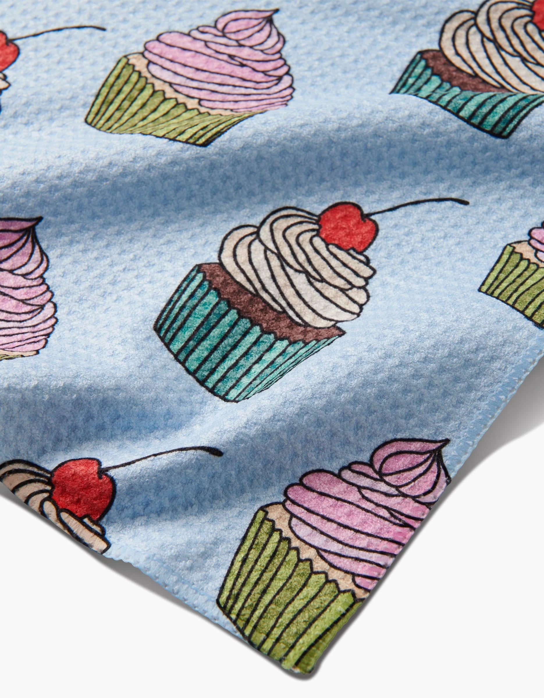 Cupcake Love by Amy Droubay: a blue Geoweave fabric bar towel with a repeating pattern of cupcakes in green or turquoise wrappers, topped with pink or white swirled frosting and cherries.