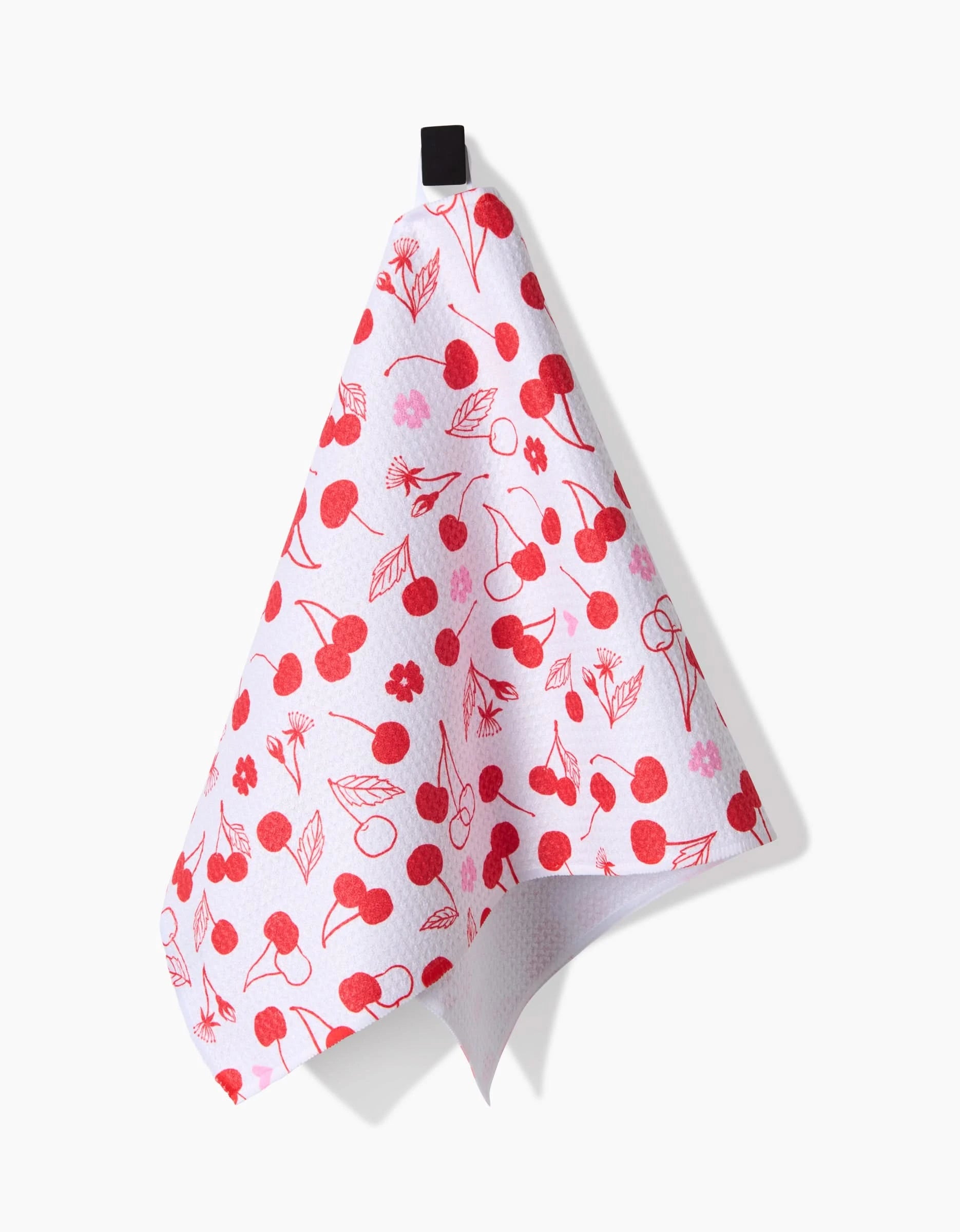 The Cute Cherry ultra-absorbent white bar towel from Elana Gabrielle, featuring a red cherry and leaf pattern, hangs from a black loop against a plain white background.