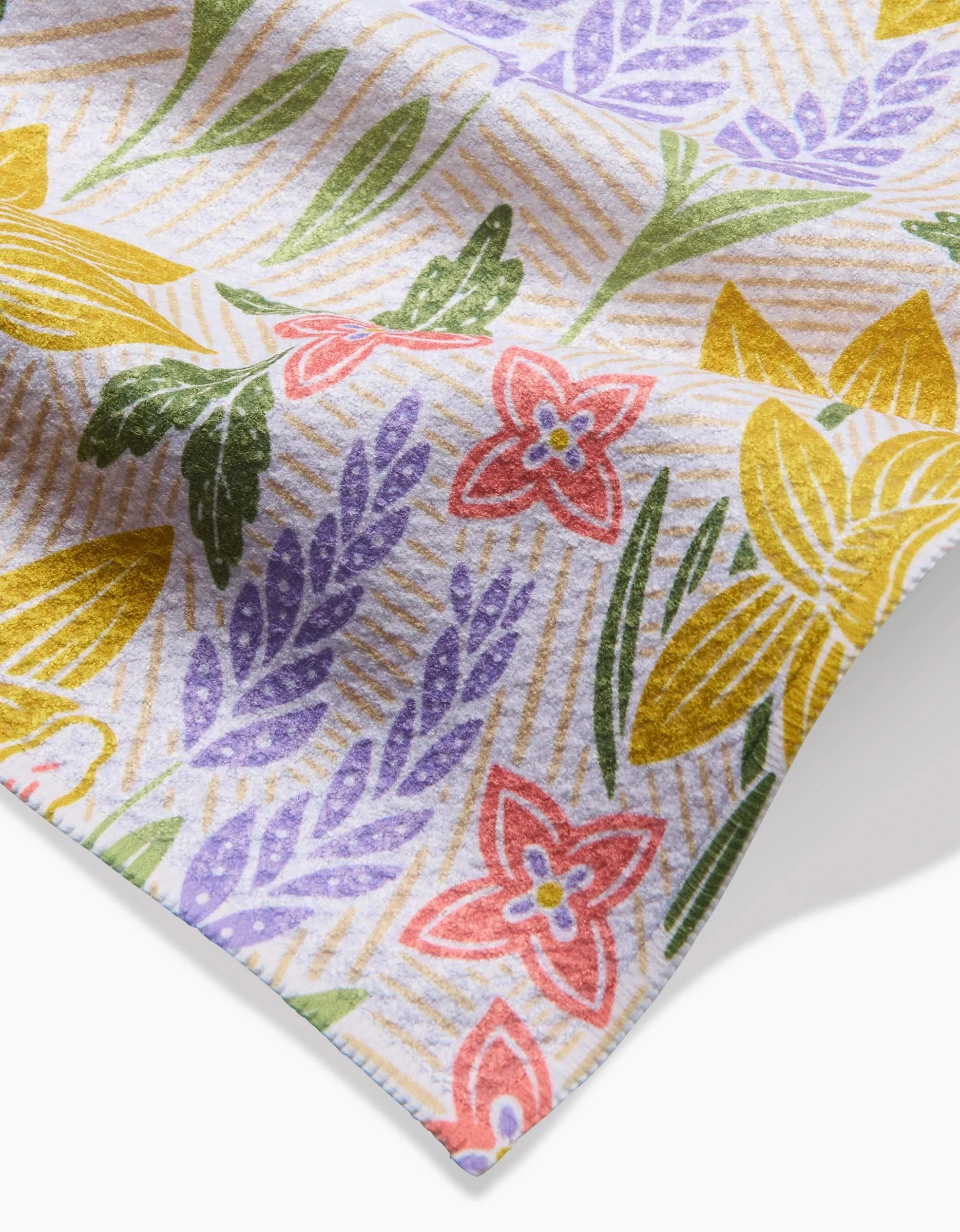 A close-up of Sarah Daugherty’s Daffodil Dreams, a soft Geoweave fabric with a colorful floral pattern—red, yellow, and purple flowers with green leaves on a light background featuring diagonal lines.
