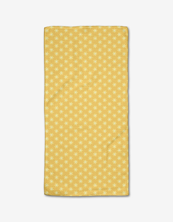 The Rebecca Bobko Daisy Daze bar towel features a yellow background with small white flowers, crafted from ultra-absorbent Geoweave fabric and displayed on a white surface.