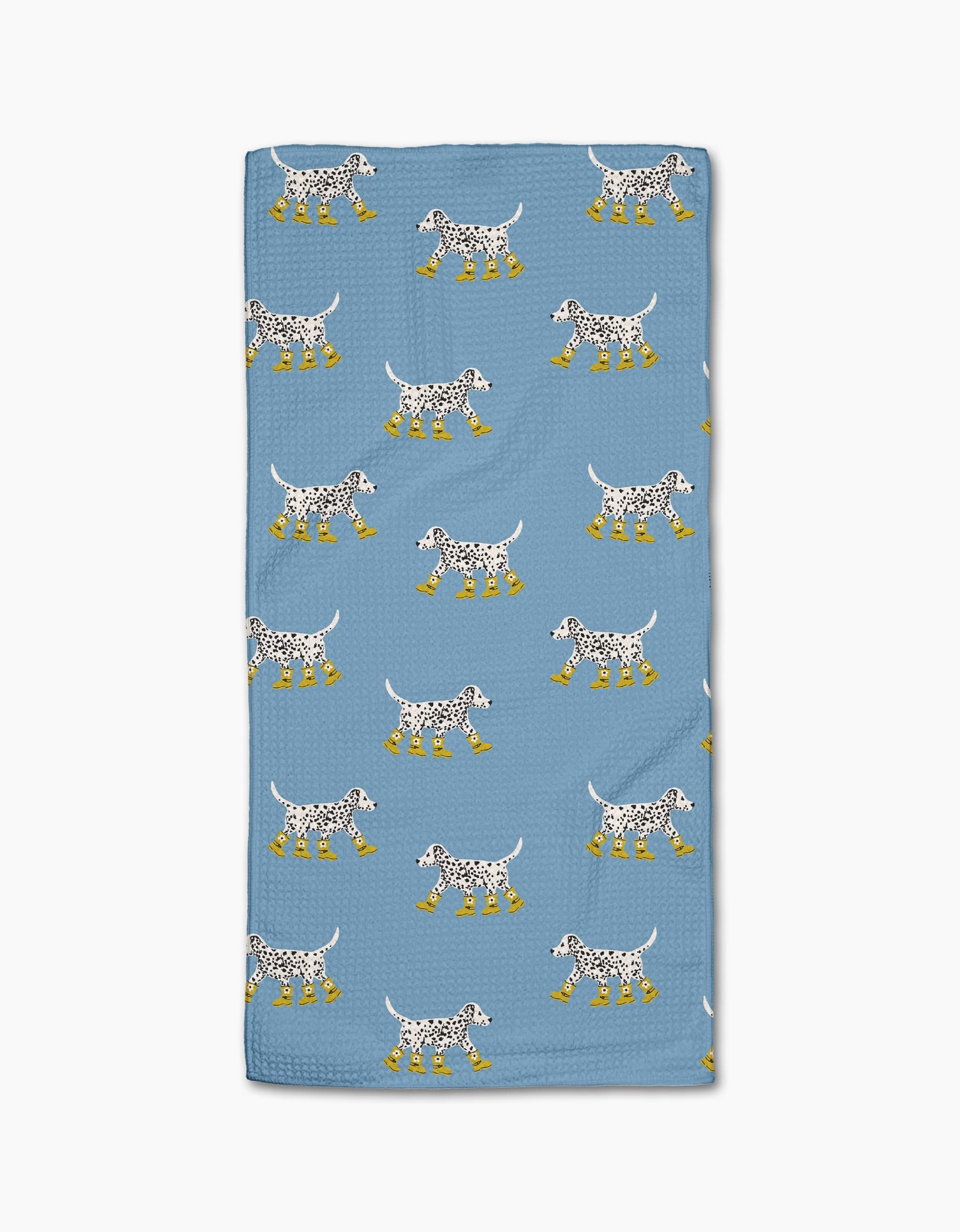 Geometry’s “Dalmatian In Boots Blue” towel features a blue, ultra-absorbent design with cartoon Dalmatian dogs in yellow rain boots on a white background.