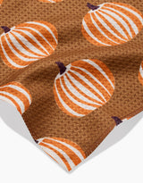The Dancing Pumpkins bar towel by Lizzie Clark features a brown textured Geoweave fabric with a repeating pattern of orange and white pumpkins and dark brown stems, made from recycled materials and shown on a white background.