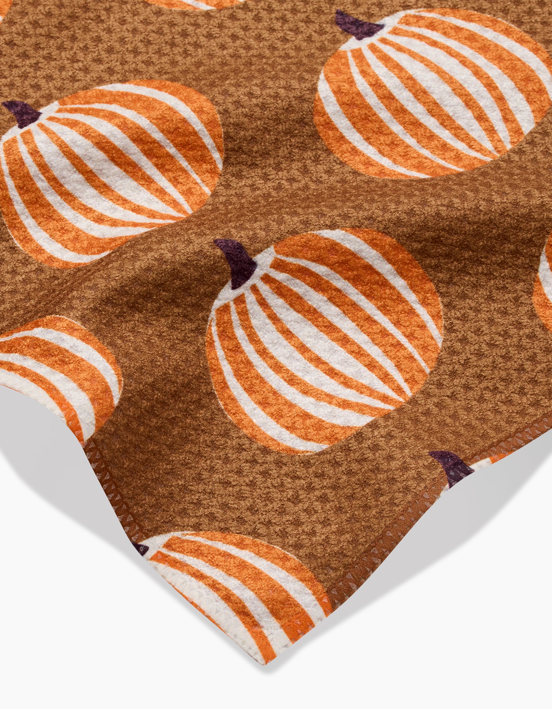 The Dancing Pumpkins bar towel by Lizzie Clark features a brown textured Geoweave fabric with a repeating pattern of orange and white pumpkins and dark brown stems, made from recycled materials and shown on a white background.