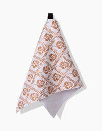 The Dancing Vines towel by Charlie Rowan Designs features a white, ultra-absorbent fabric with a brown leaf and floral pattern, hanging from a black loop against a plain white background.