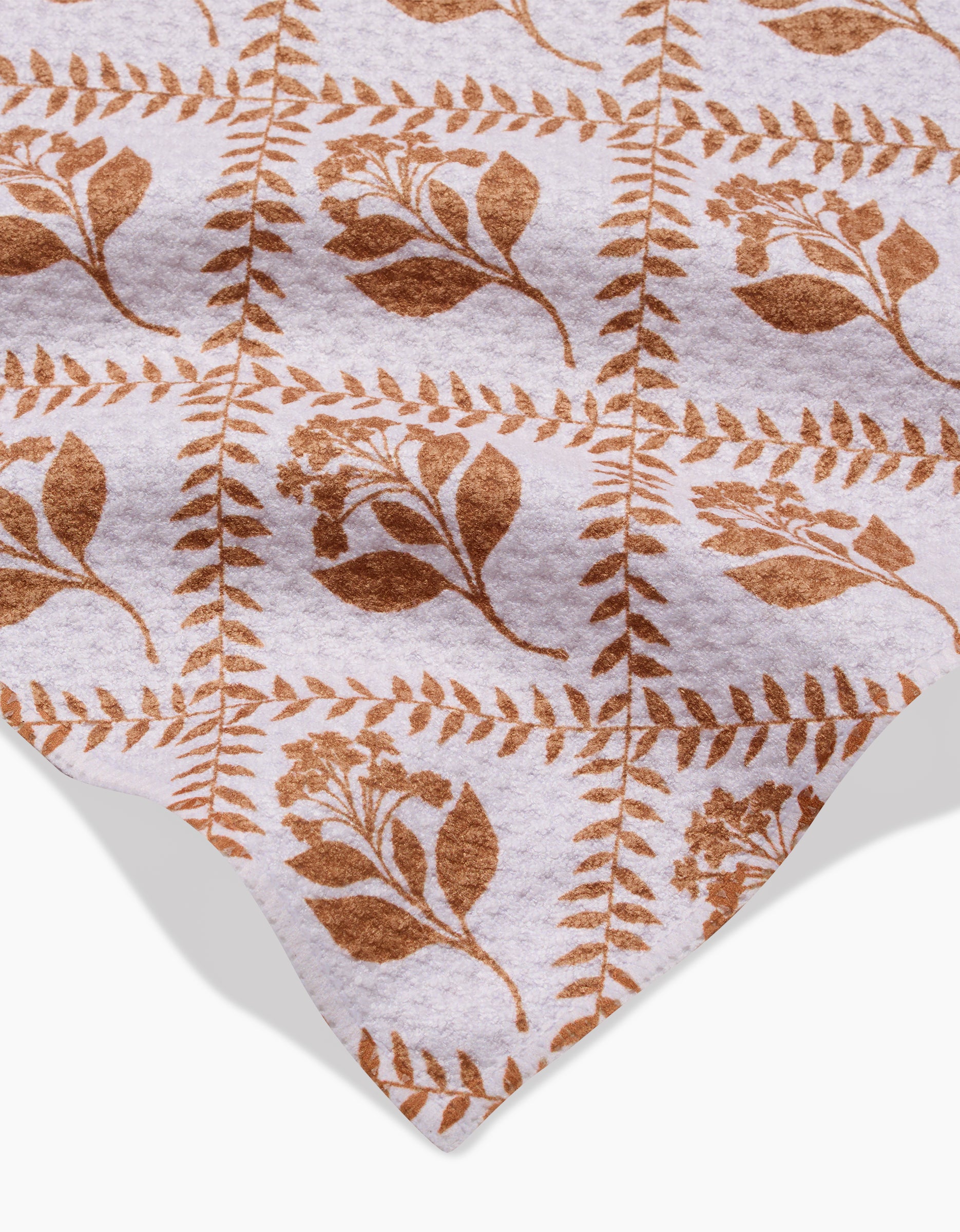 The Dancing Vines towel by Charlie Rowan Designs features a soft, ultra-absorbent fabric with brown botanical leaves and flowers in a grid on a white background, showcased with its finished edge in the corner.