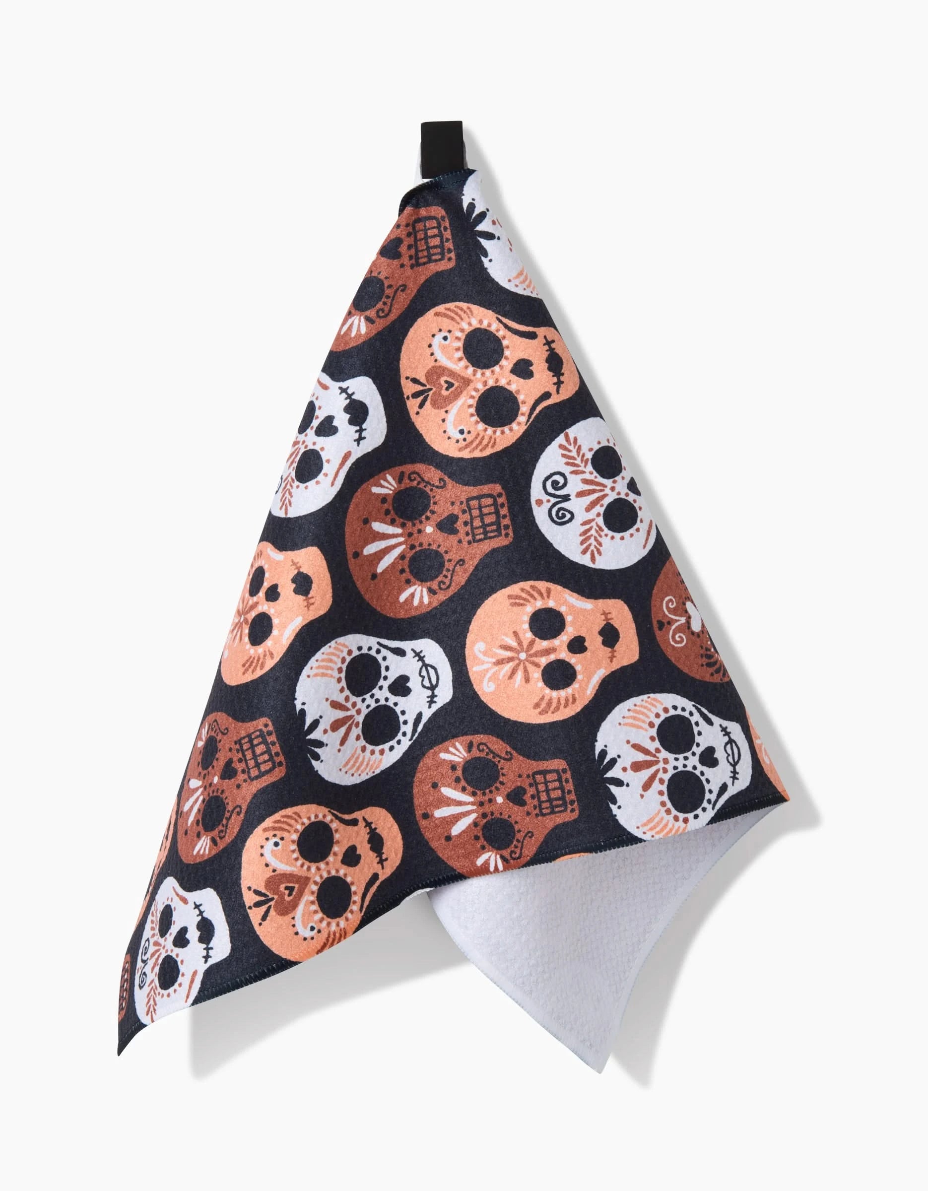 The Hufton Studio Day Of The Dead Skulls towel, featuring an ultra-absorbent design with orange, white, and black sugar skulls, hangs from a black loop against a plain white background.