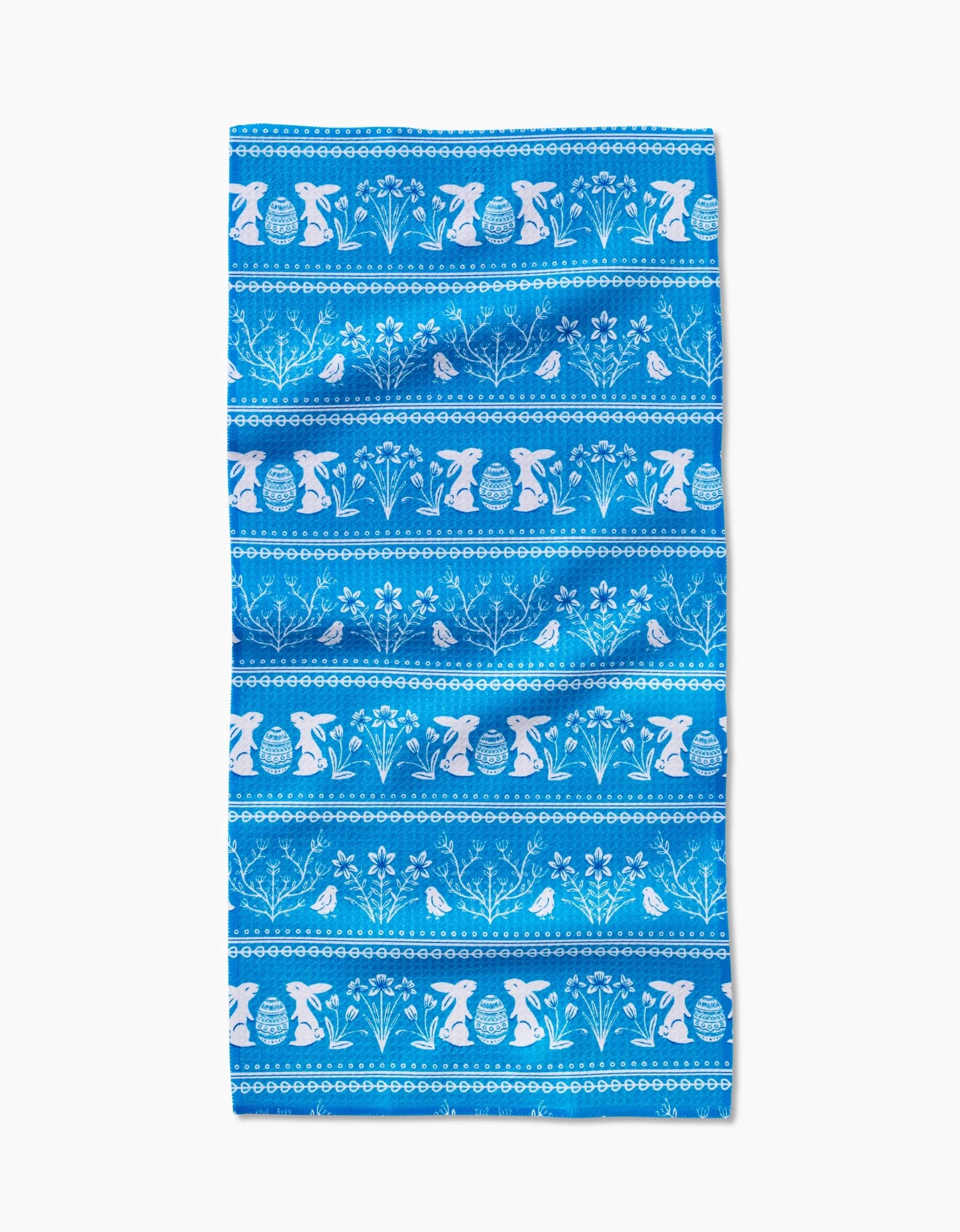 The Delft Blue Easter Stripe by Sarah Daugherty is a Geoweave napkin with blue horizontal stripes and white silhouettes of rabbits, Easter eggs, flowers, and leaves in a repeating pattern.