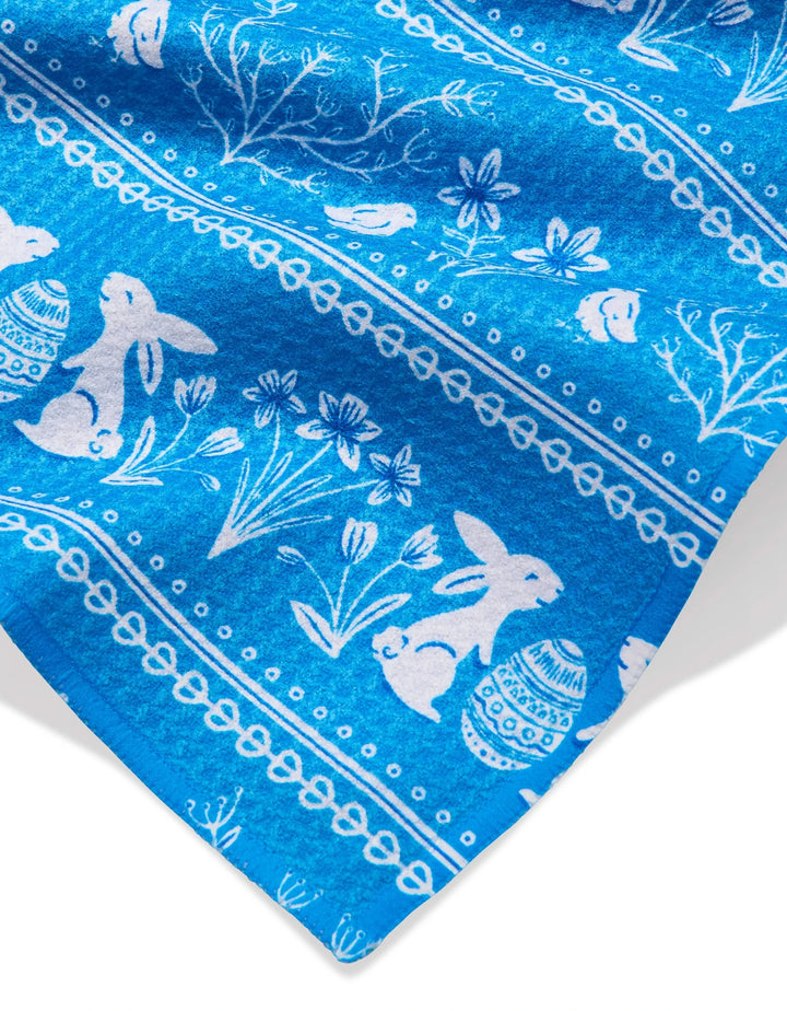 The Delft Blue Easter Stripe bar towel by Sarah Daugherty features bright blue Geoweave fabric with white rabbits, birds, eggs, flowers, and branches in horizontal rows—an elegant and festive accent for your kitchen.