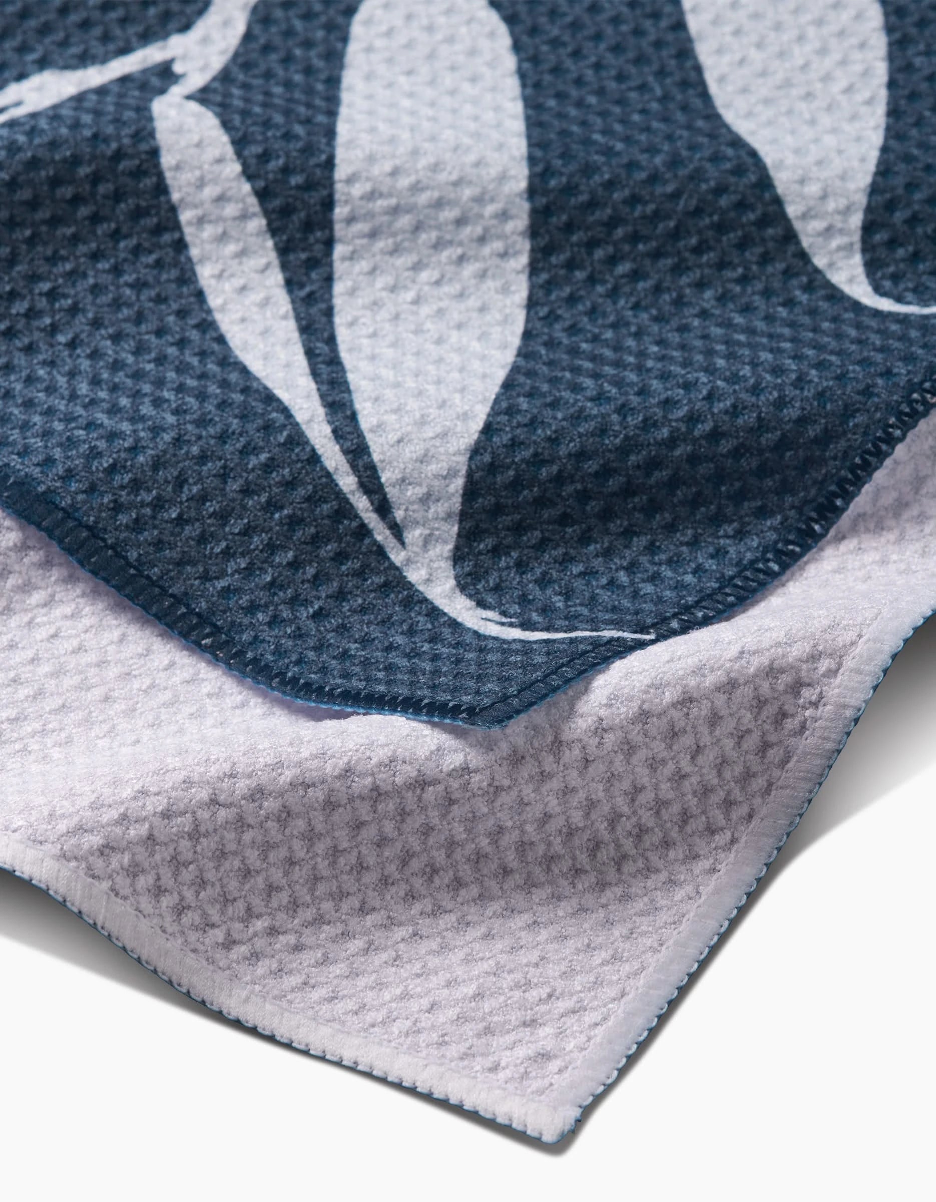 Close-up of Doghobble by PrintedPlant, showing the corner of a textured Geoweave fabric towel with a dark blue top layer featuring a white abstract pattern and a light lavender underside.