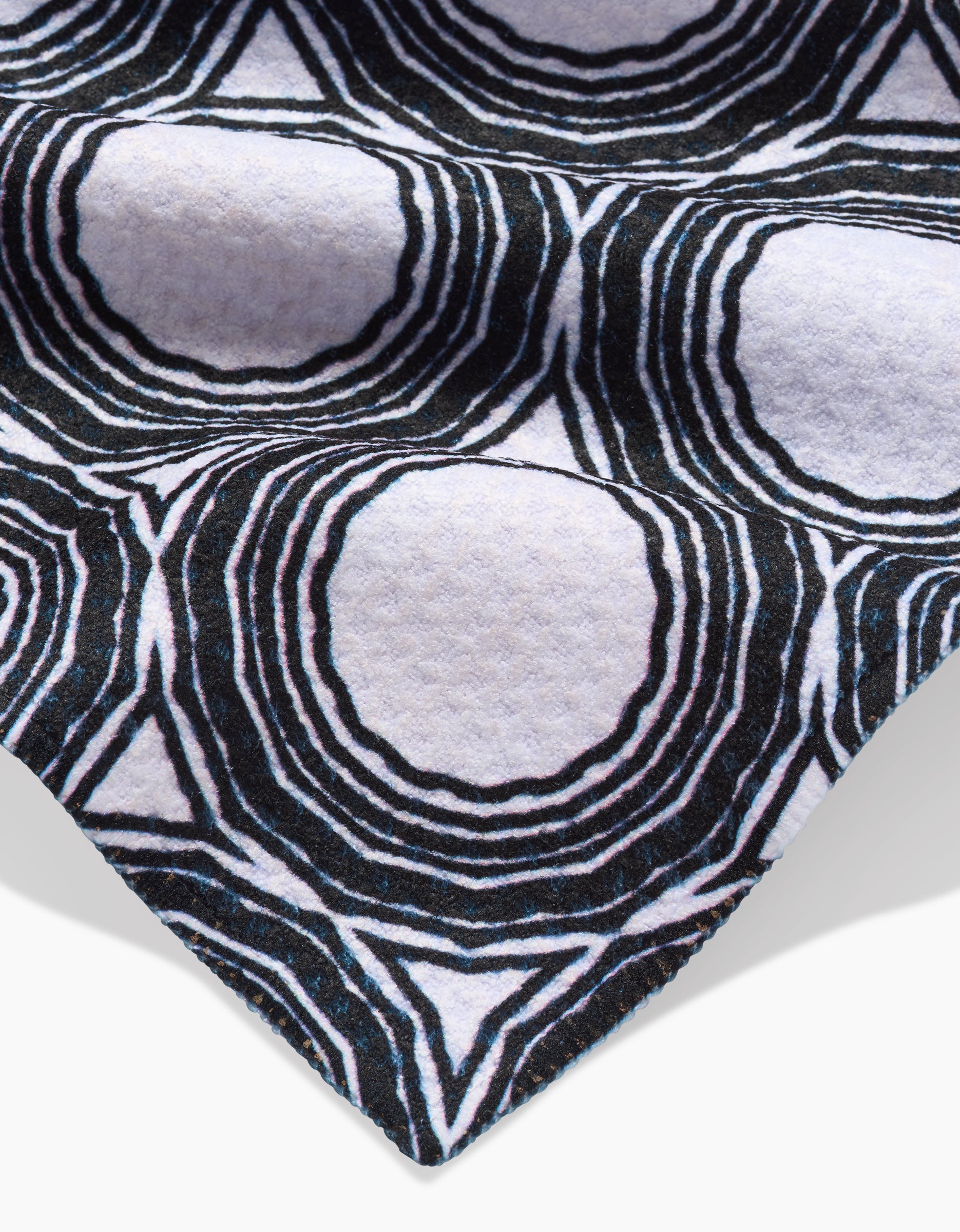 A close-up of Dosido by Katherine Berkeley shows its Geoweave fabric in a black and white concentric circular pattern, giving a textured, almost 3D look. The edge of this ultra-absorbent bar towel is visible in the lower corner.