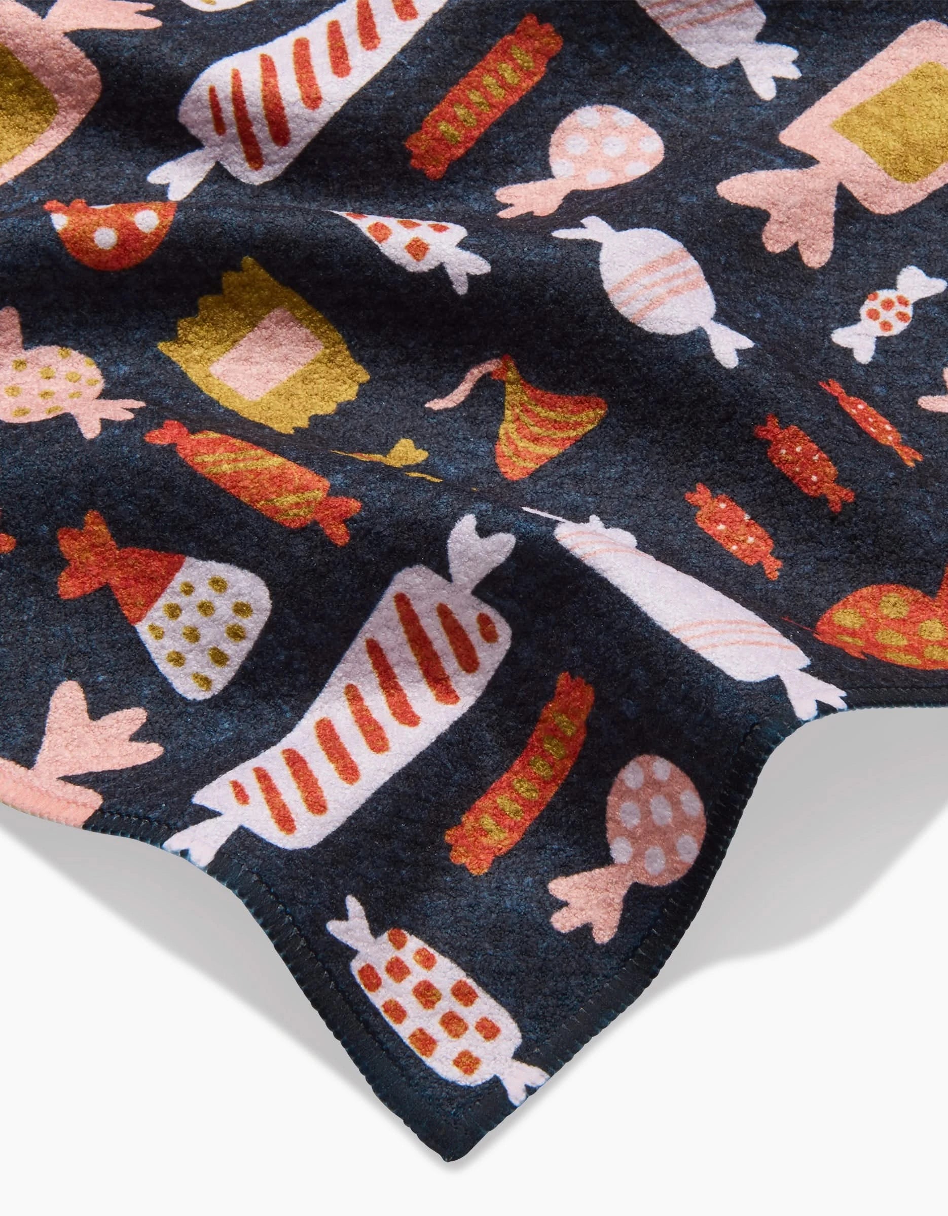 The Edwina by Amy MacCready is a dark fabric blanket with vibrant candy patterns in red, pink, yellow, and green, finished with a playful zigzag border for extra style.