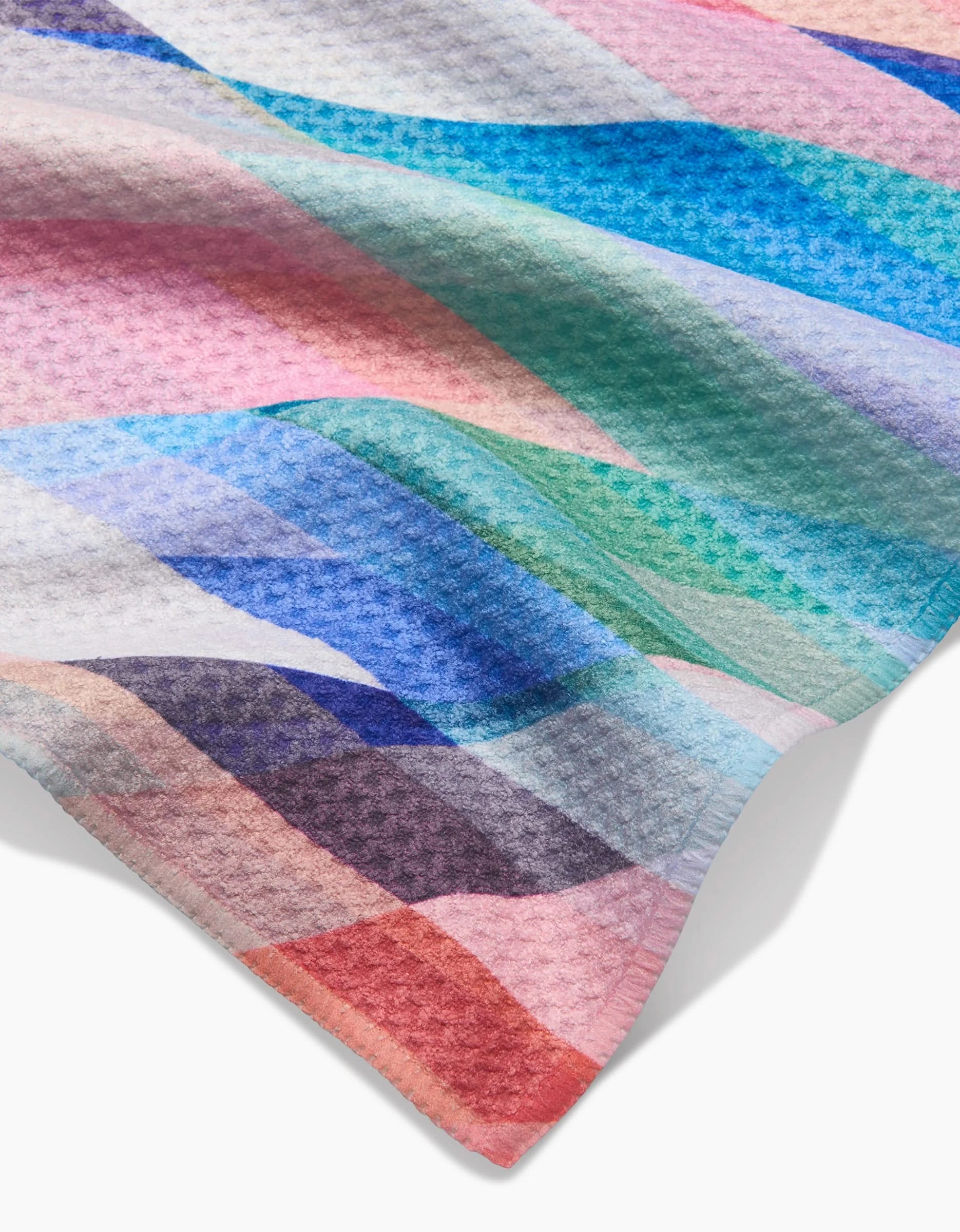 A close-up of the Eventide Bar Towel by Rachel Parker, featuring a colorful wavy pattern in blue, pink, purple, teal, and white. Its Geoweave fabric and waffle texture highlight its eco-friendly and unique design.