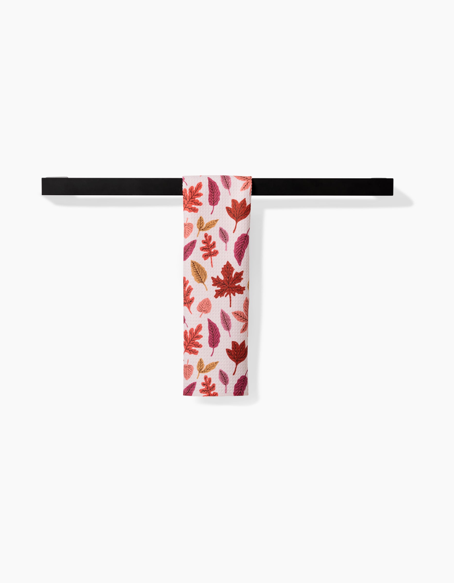 The Kayla Ann Fall Leaves bar towel, featuring red, orange, and purple autumn leaf patterns on white Geoweave fabric for absorbency and durability, hangs neatly on a modern black towel bar against a plain white background.