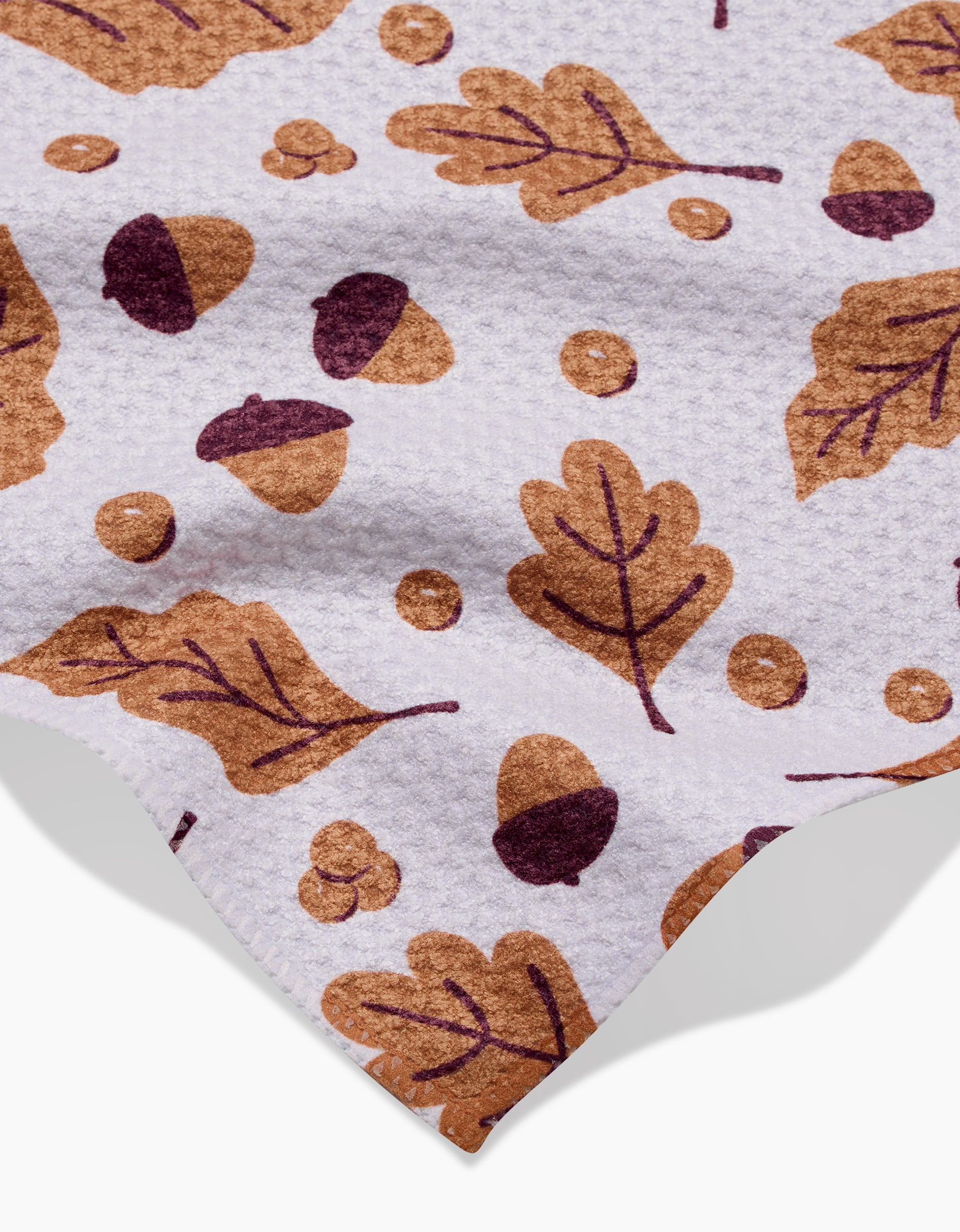 Falling For Fall by Charlie Rowan Designs is a white textured recycled kitchen towel featuring brown and dark purple acorns, oak leaves, and berries, with part of the cloth edge visible.
