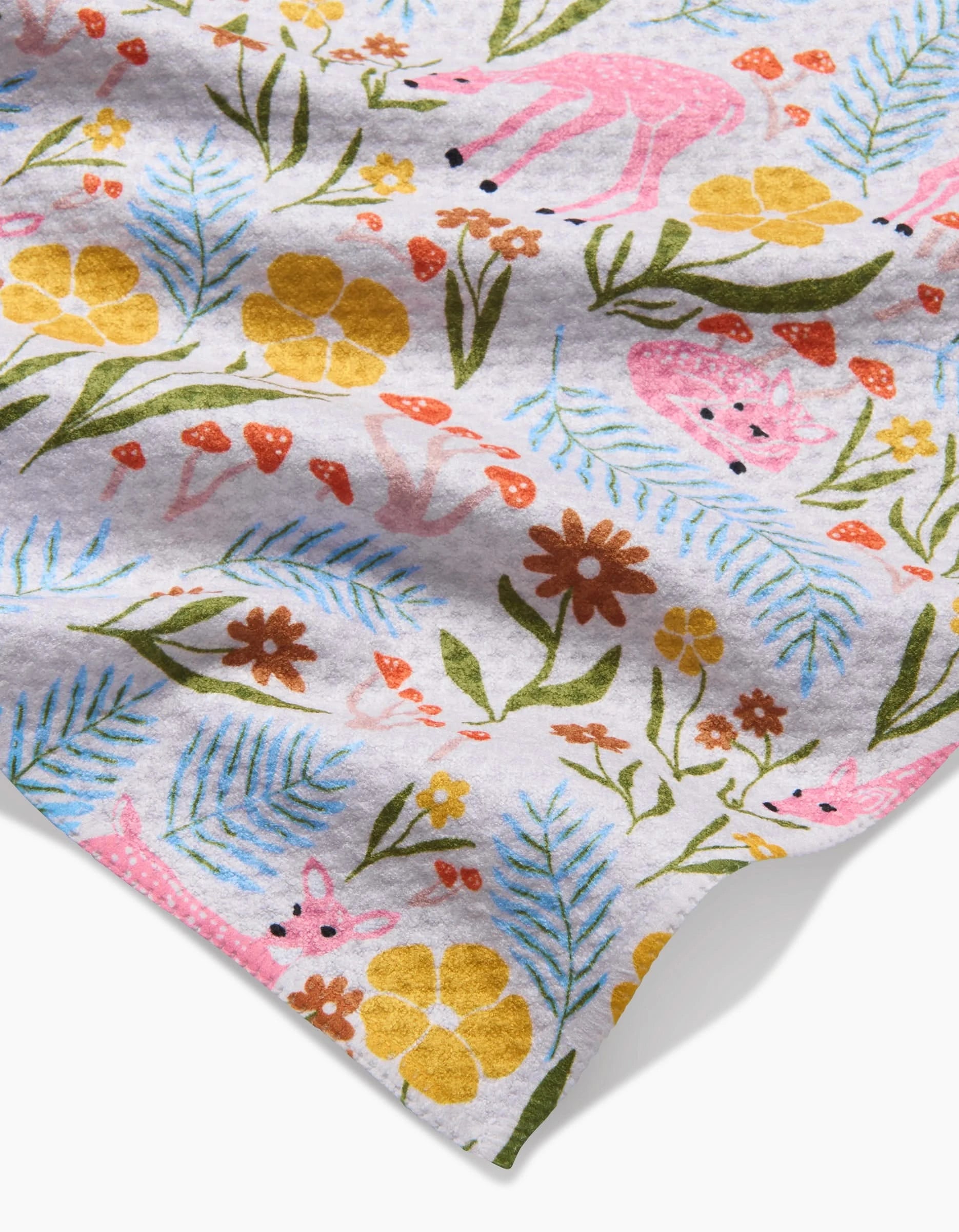The Fern and Fawn bar towel by Kayla Ann features a whimsical forest pattern—pink deer, yellow and orange flowers, red mushrooms, and green leaves—on Geoweave fabric made from recycled materials.