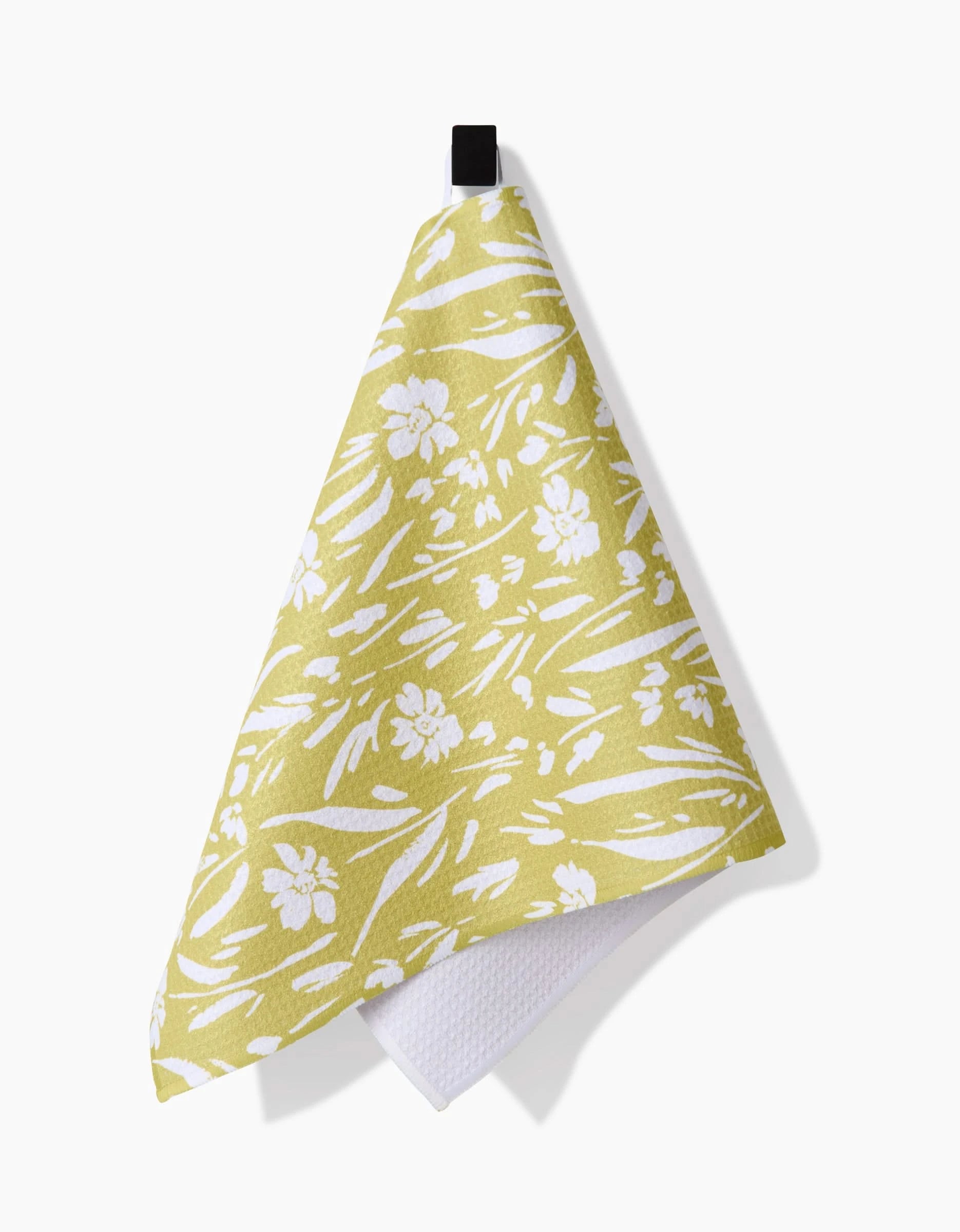 The Field of Wildflowers dish towel by Ashley Celena, featuring a yellow and white floral design and made from recycled materials, hangs from a black hook against a white background.