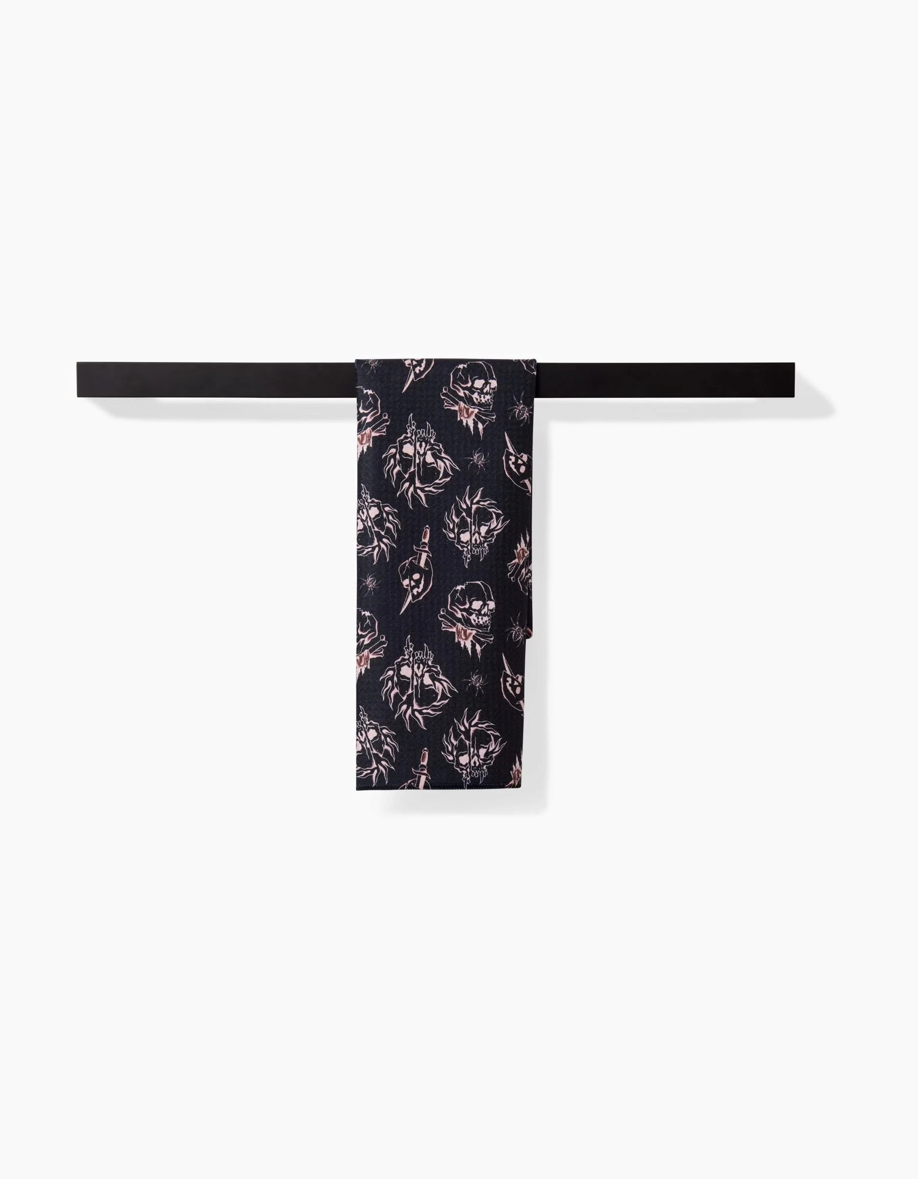 The Cole Strem Fiery Skulls bar towel, ultra-absorbent and dark with a bold skull pattern, hangs neatly on a black towel bar against a white background.