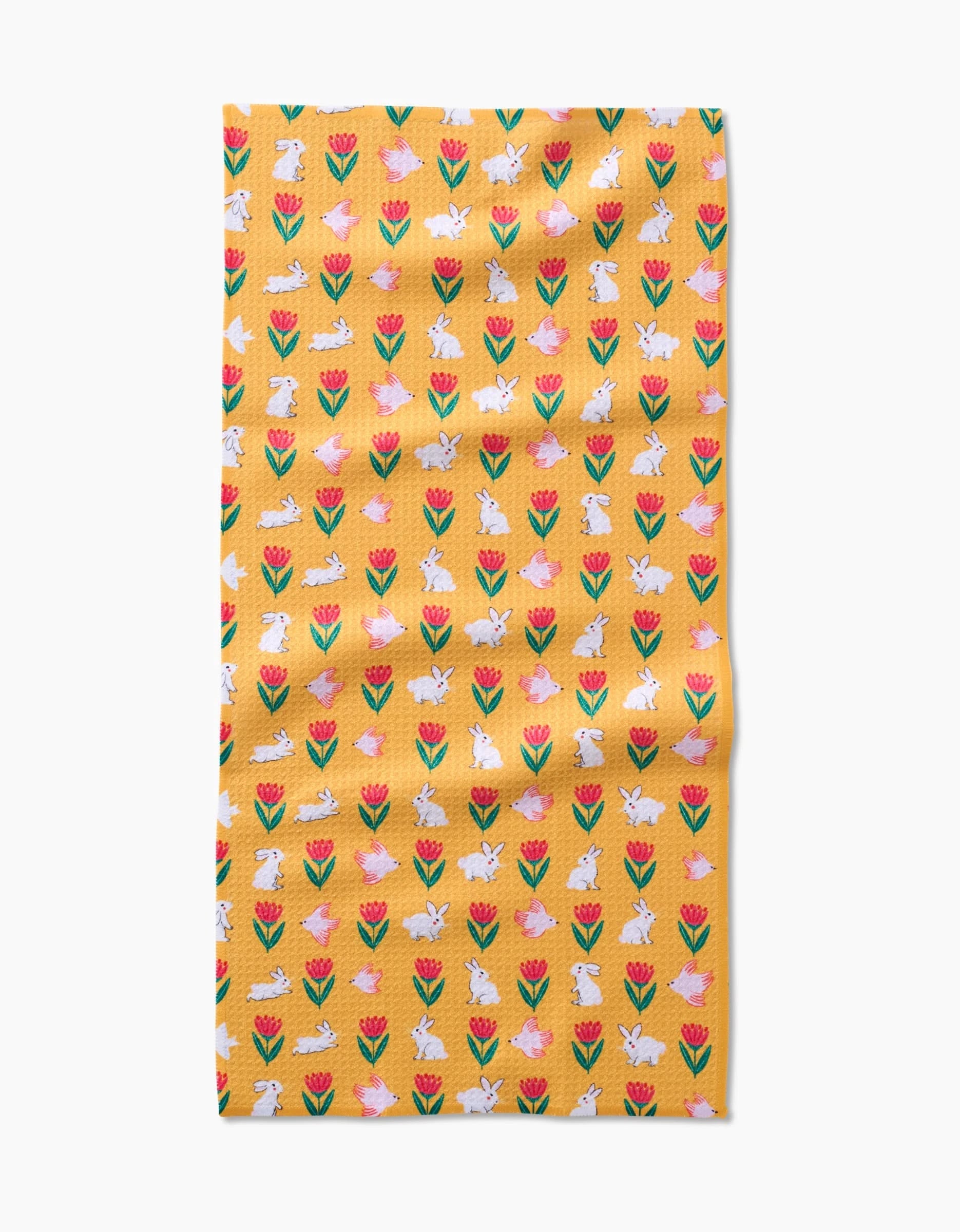 The Floral Bunny Parade kitchen towel by Ceyda Alasar features a yellow recycled fabric with red and pink tulips and white bunnies in a repeating pattern, shown slightly wrinkled on a white background.